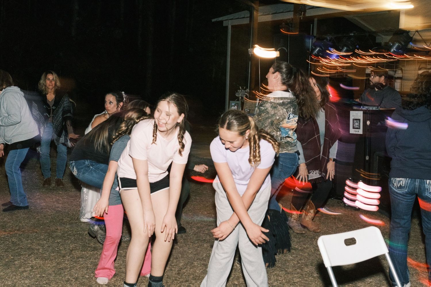 Children dance and play with glow sticks at an outdoor evening wedding reception celebration.