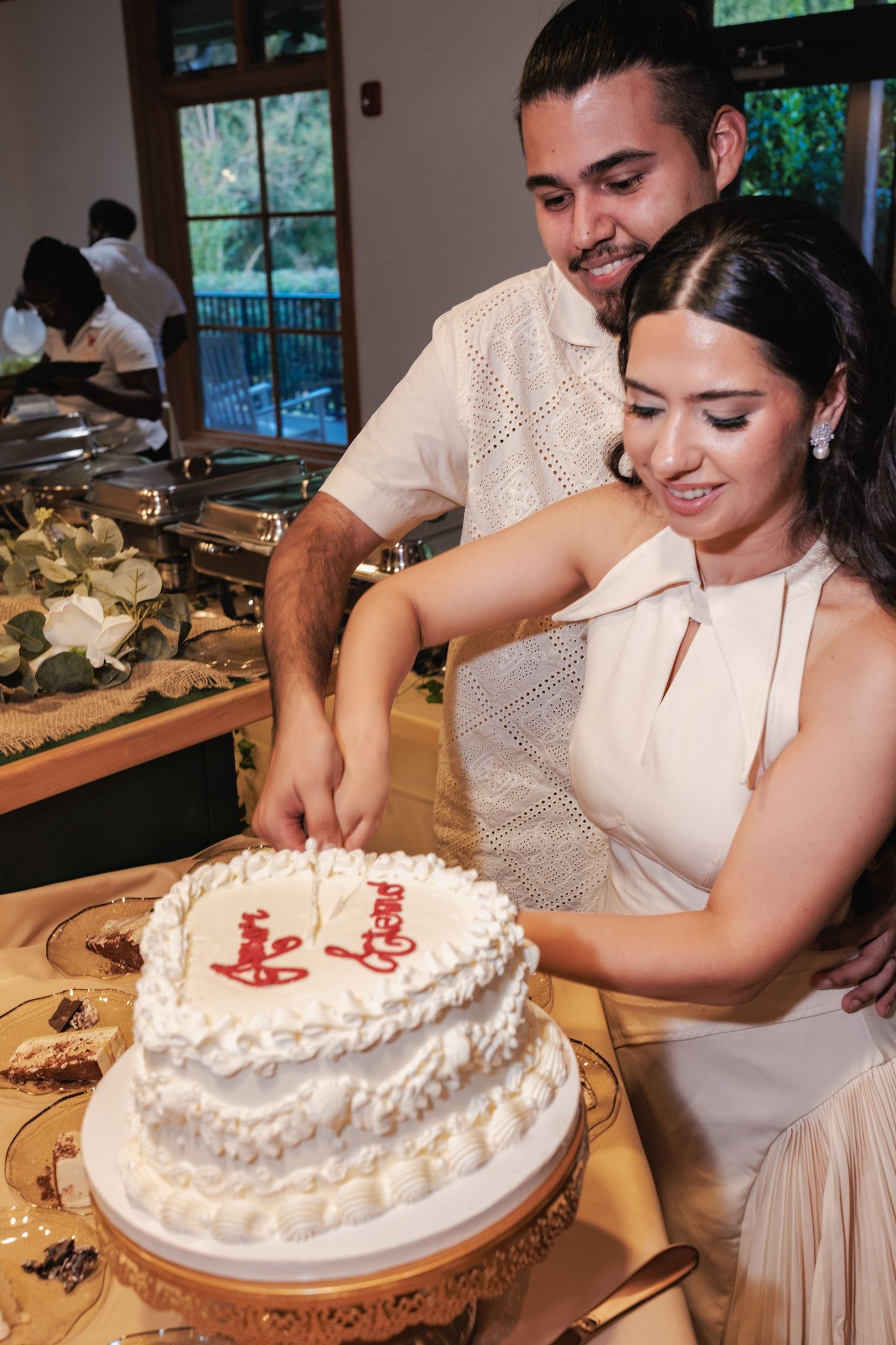 White wedding cake with decorative frosting being cut at reception.