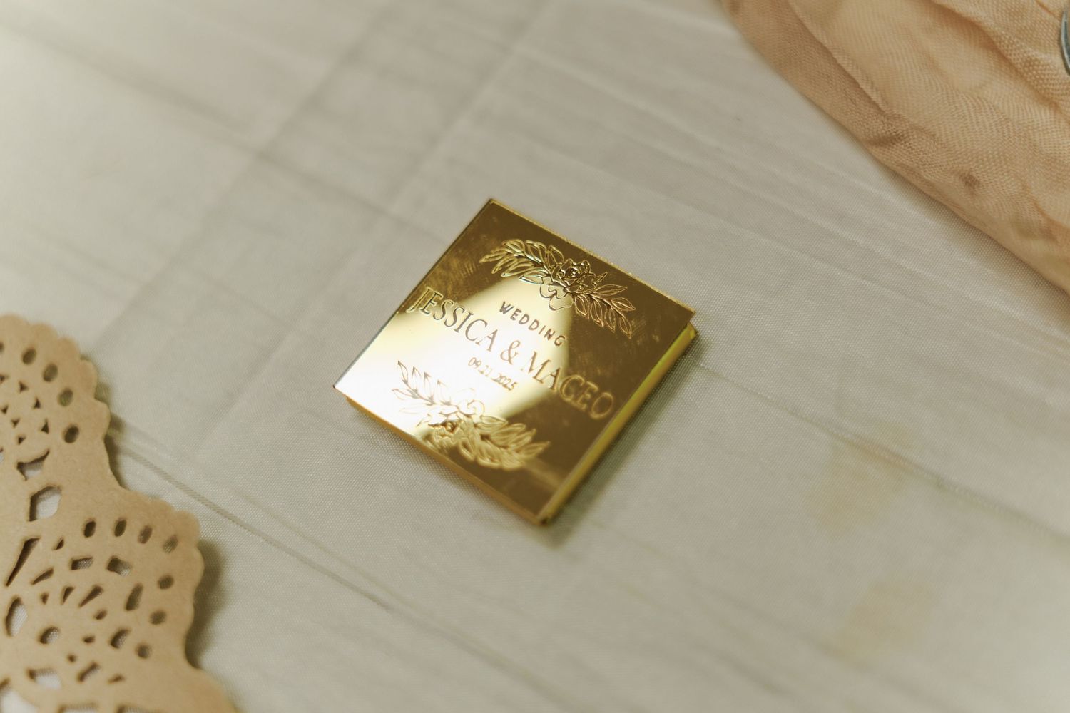 Close-up of gold foil wedding invitations and delicate paper details on a light wooden surface.