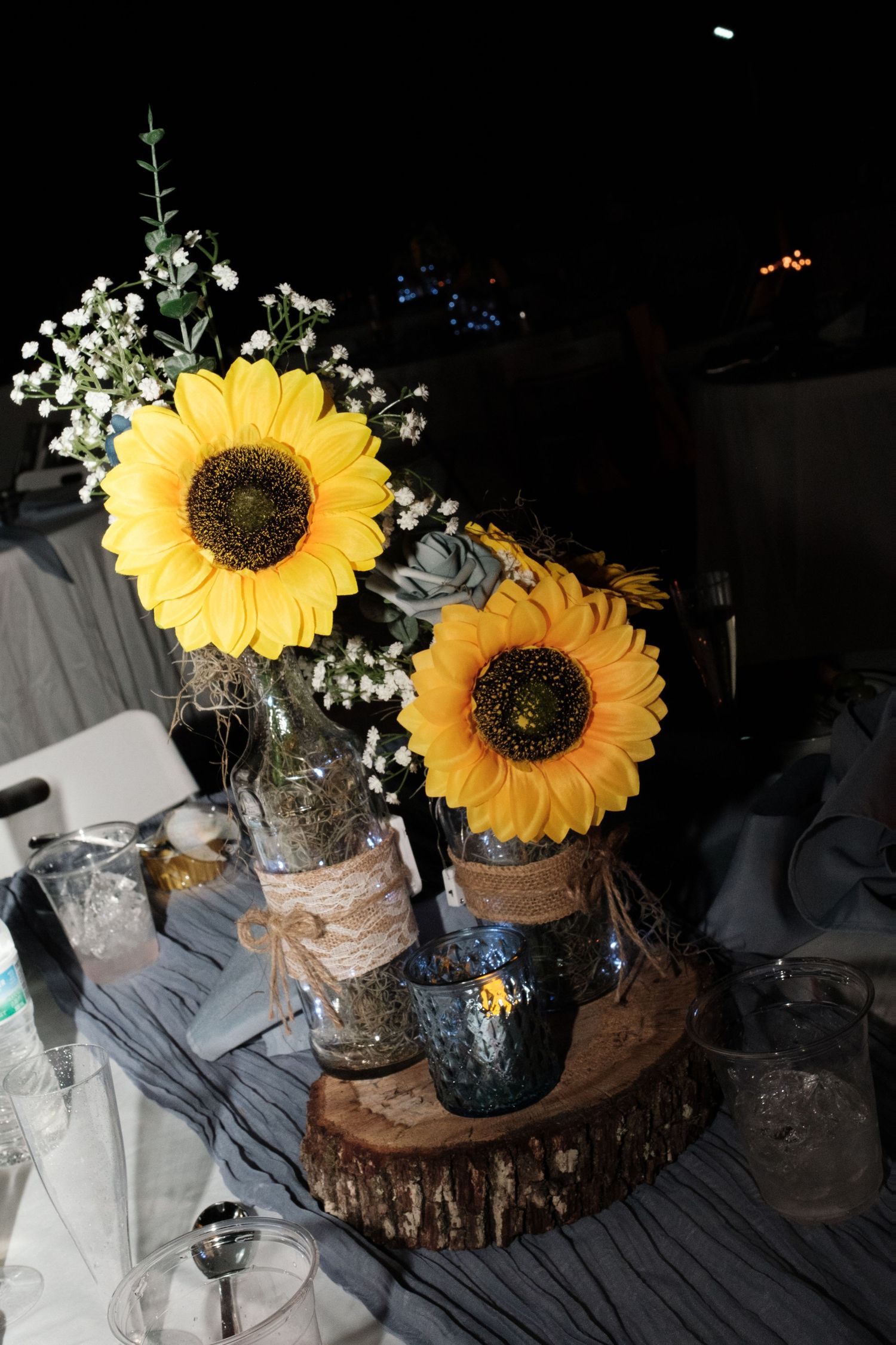 Sunflower centerpiece in mason jars on wood slice with baby's breath at wedding reception.