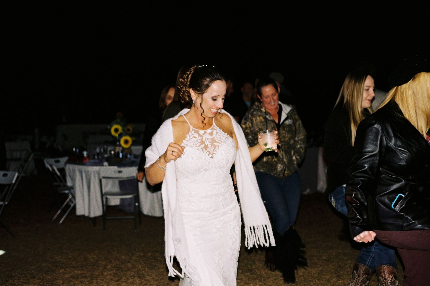 Bride in white lace gown and fringed shawl dances at nighttime outdoor wedding reception.