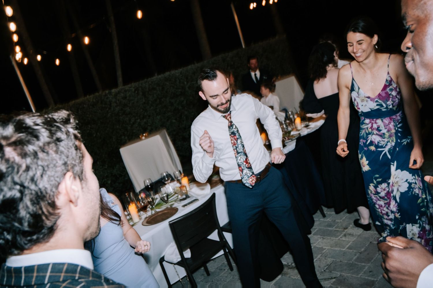 Wedding reception guests celebrating and dancing under twinkling lights at night.