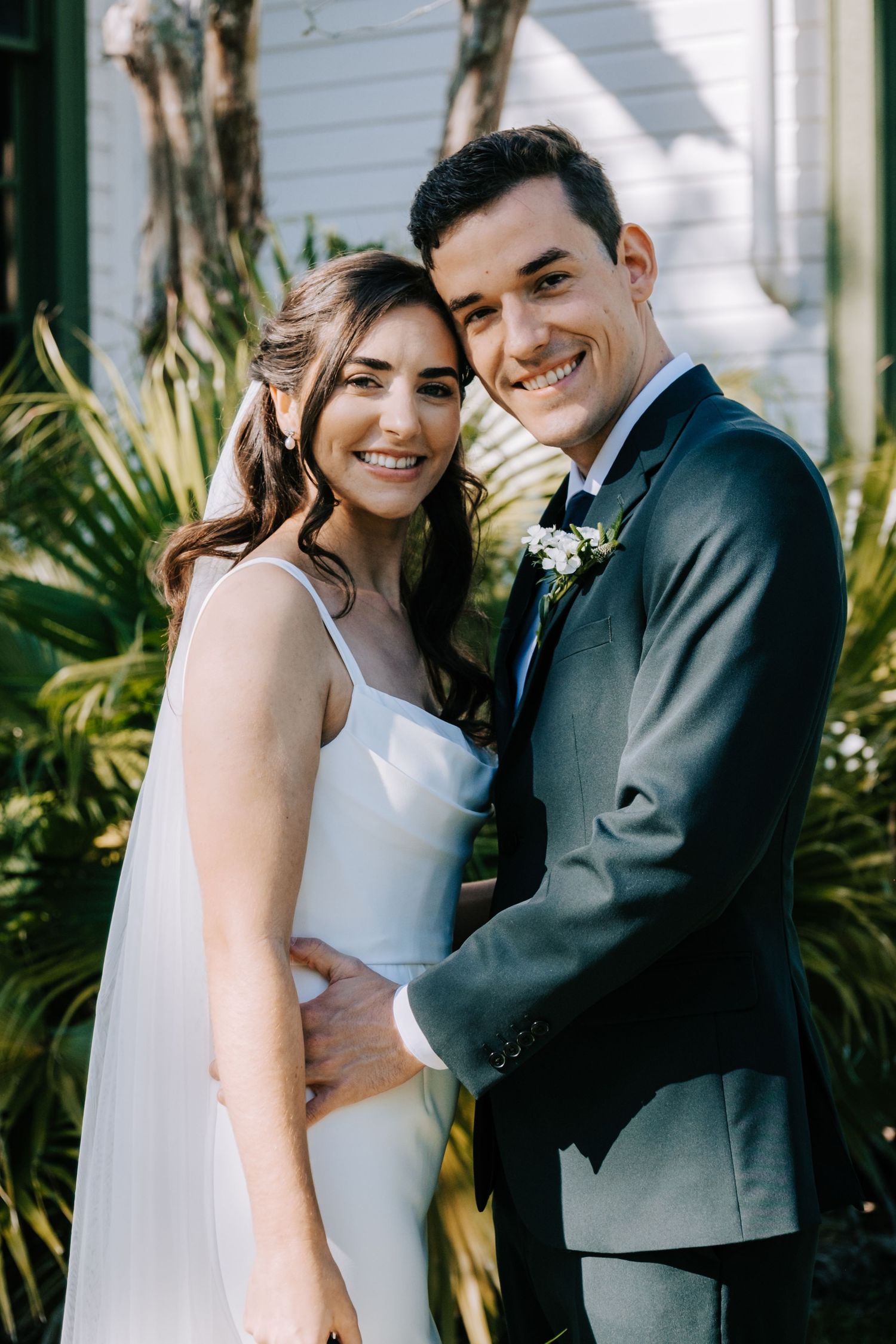 Newlyweds share joyful moments together against a backdrop of tropical plants.