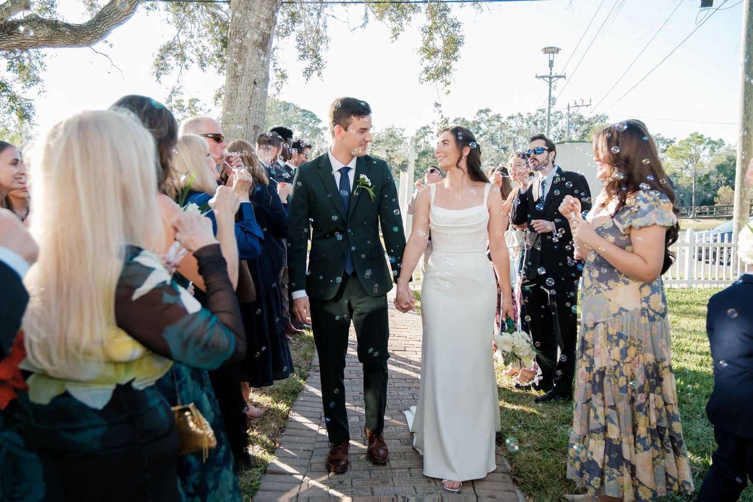 Outdoor wedding celebration with guests throwing confetti under oak trees.