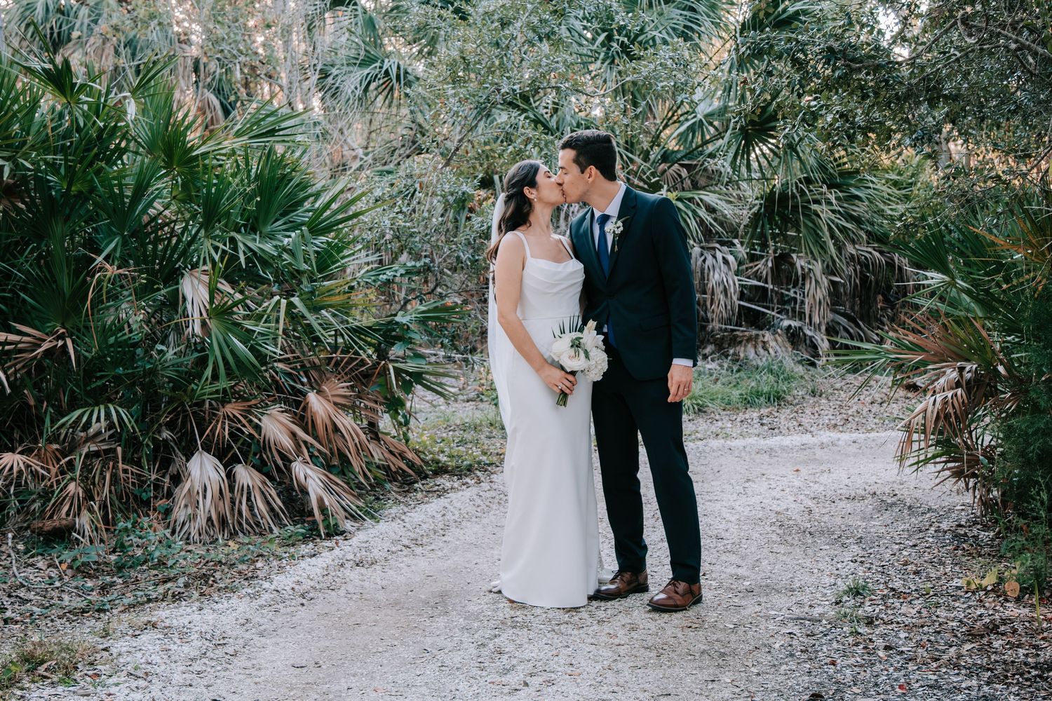 A couple shares a romantic moment on a path surrounded by palm trees.