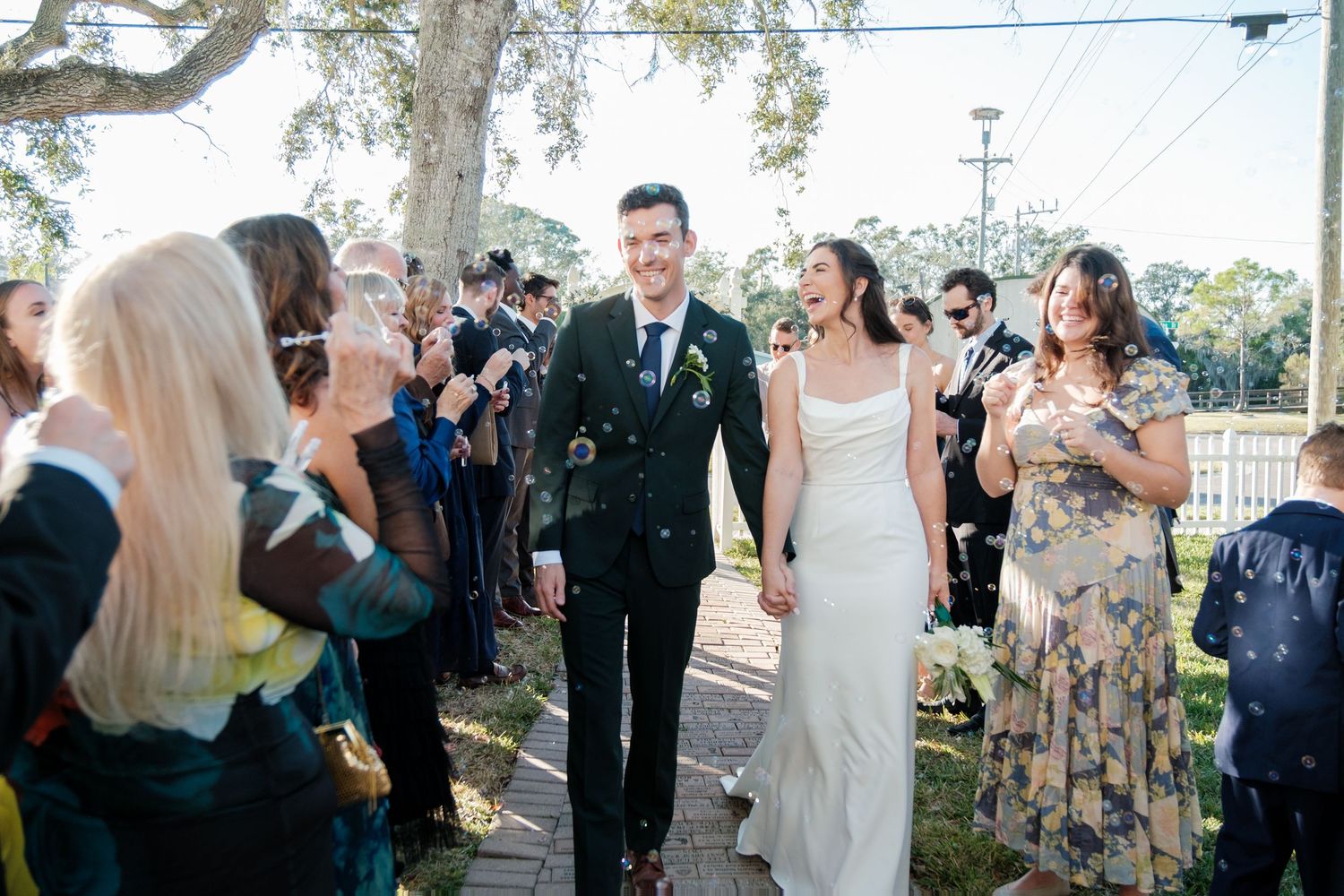 Wedding party poses under a large oak tree during an outdoor ceremony at a scenic venue.