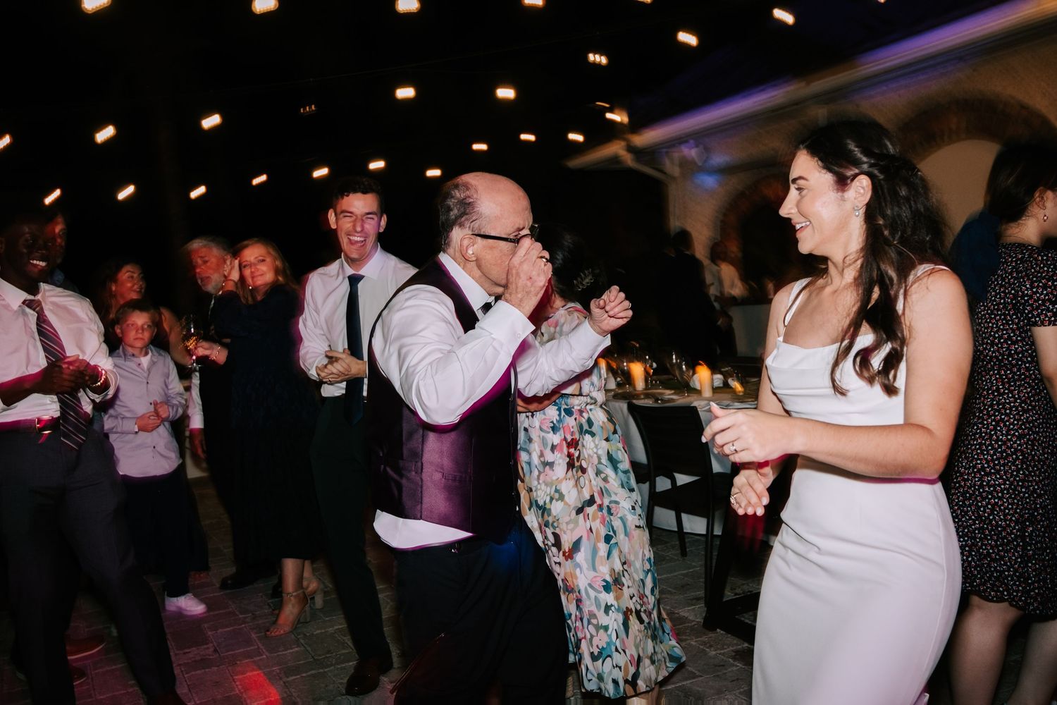 Guests dancing and celebrating at a wedding reception under ambient lighting.