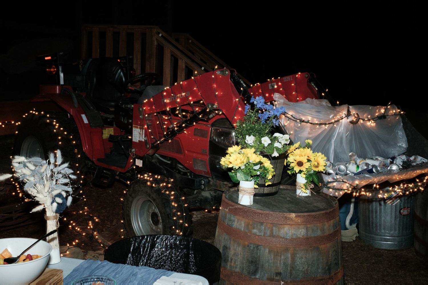 Rustic wedding reception decor featuring a tractor wrapped in string lights and barrel centerpieces.
