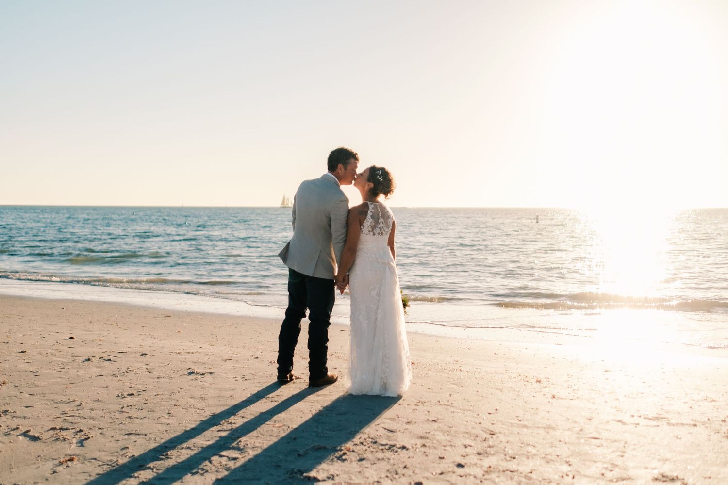 Bride and groom sharing a kiss on sandy beach with golden sunset over ocean behind them.