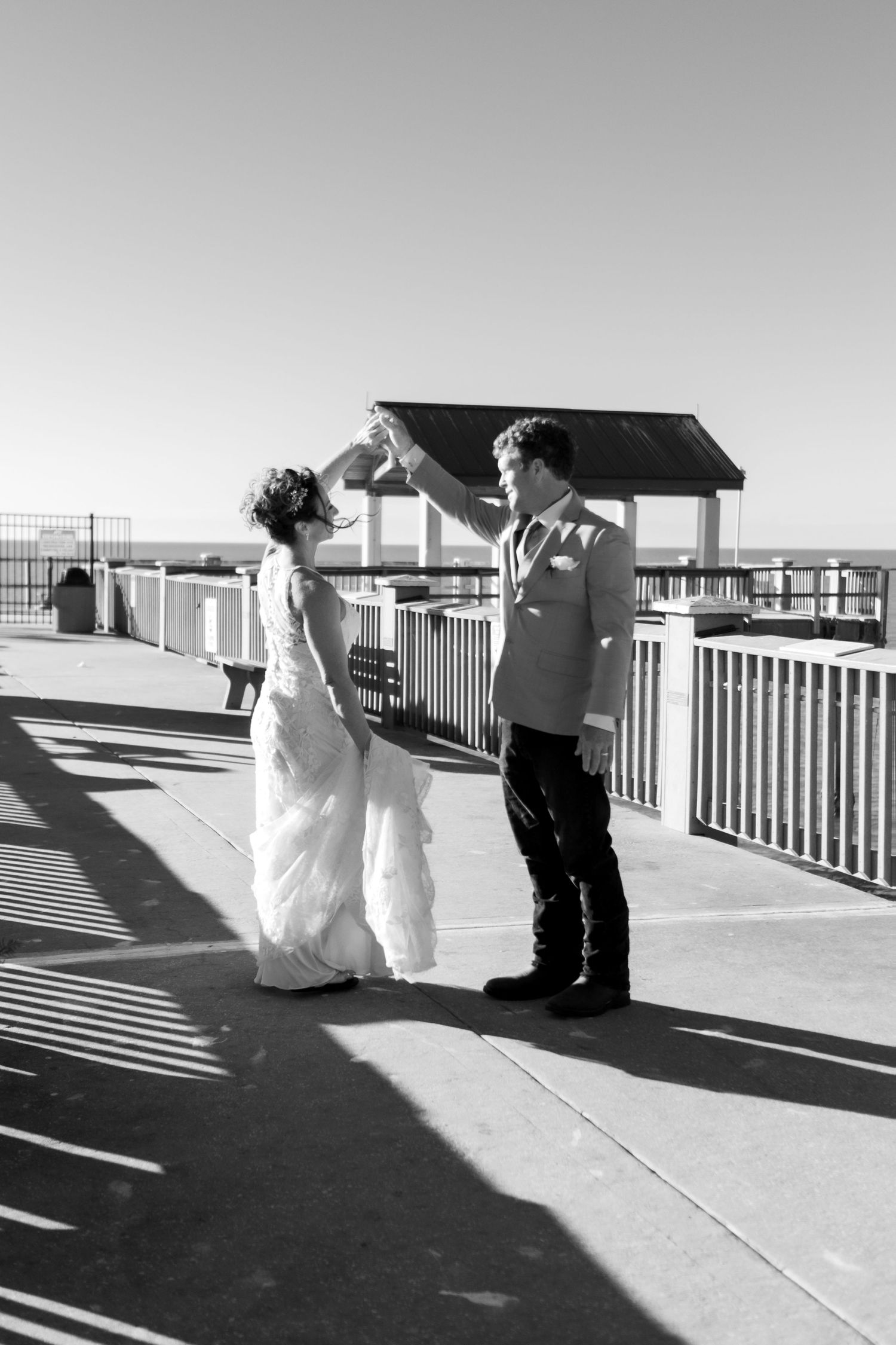 Bride and groom share a dance on an outdoor boardwalk near the water in black and white.