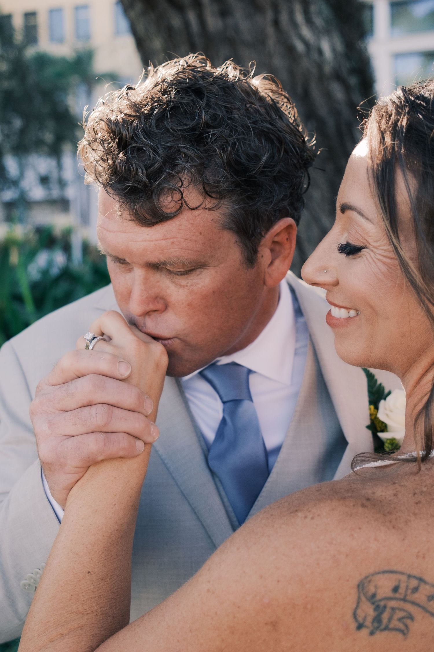 Groom in gray suit kisses bride's hand as she smiles during wedding celebration.