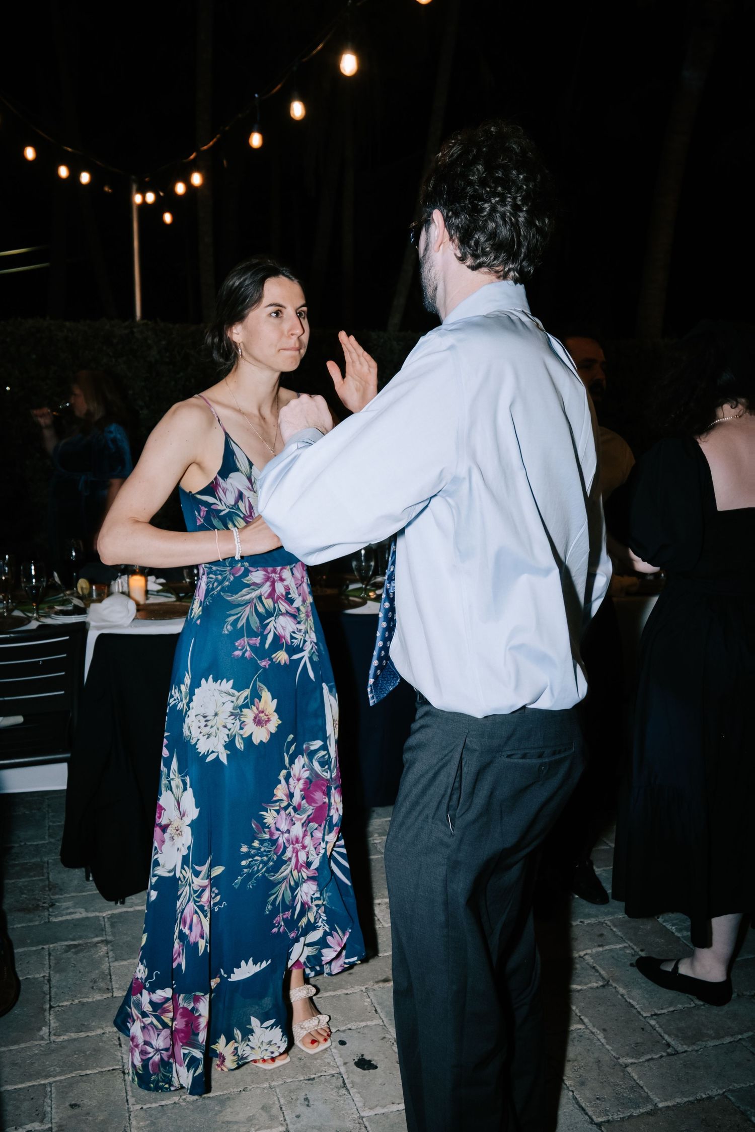 Couples dancing together at an evening wedding reception with string lights overhead.