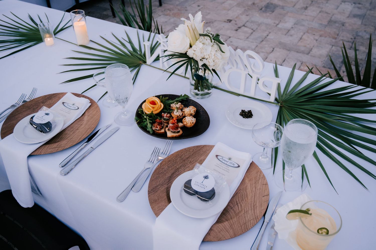 Minimalist table setting with palm fronds and wooden serving boards at tropical wedding reception.