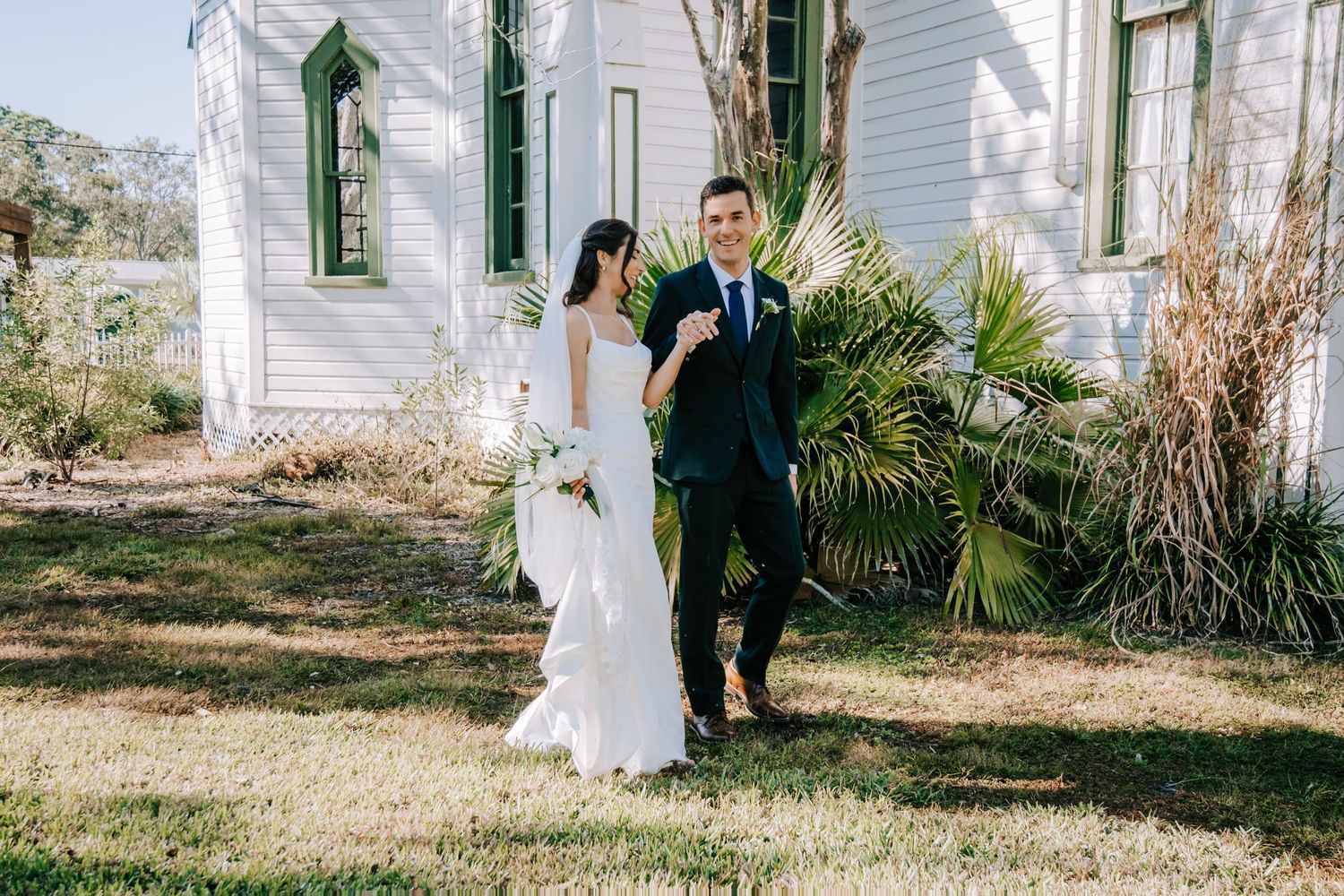 Romantic wedding first look sequence outside a white historic building with green shutters and palm trees.