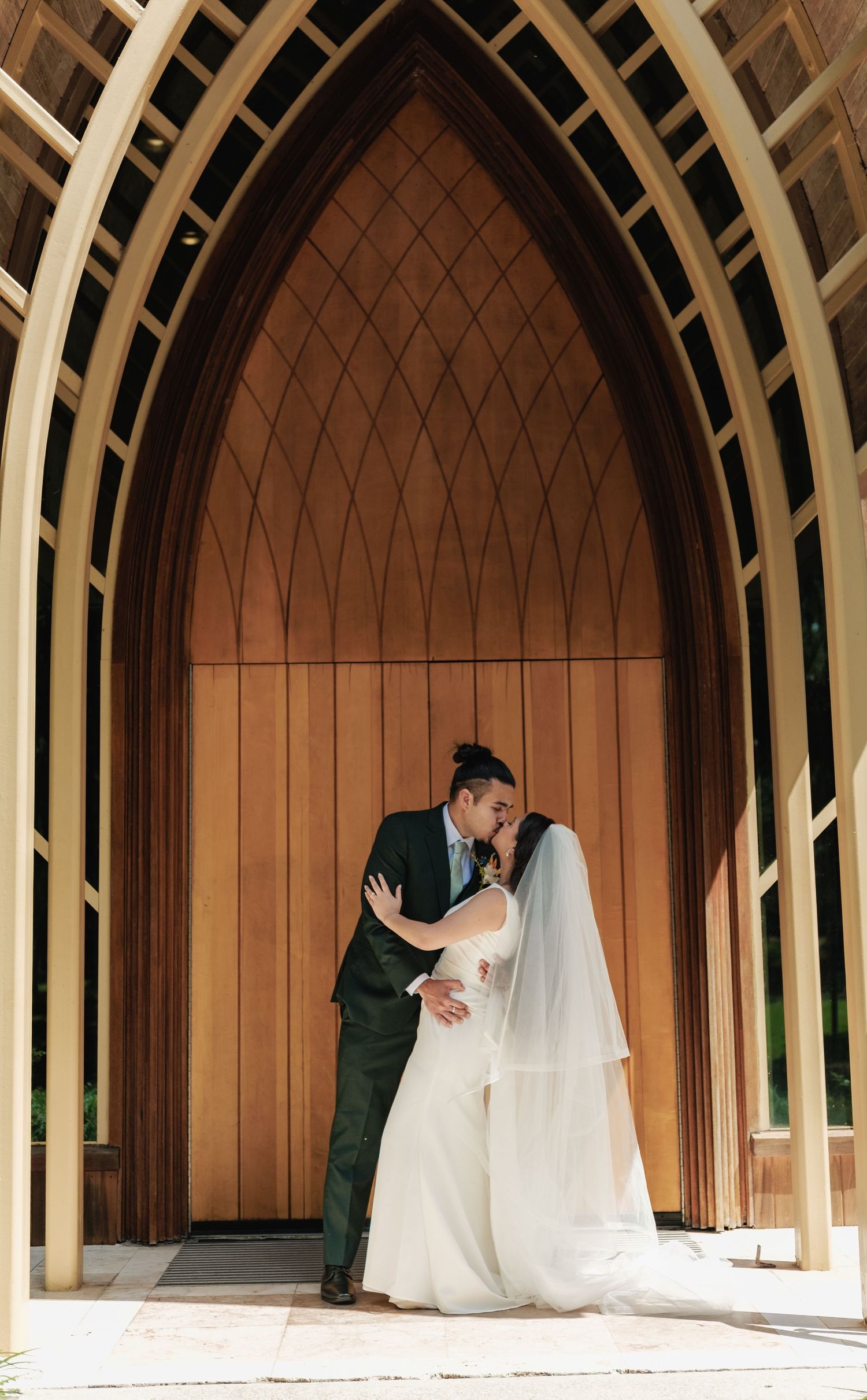 Panoramic view of wedding couple in arched wooden chapel with geometric windows.