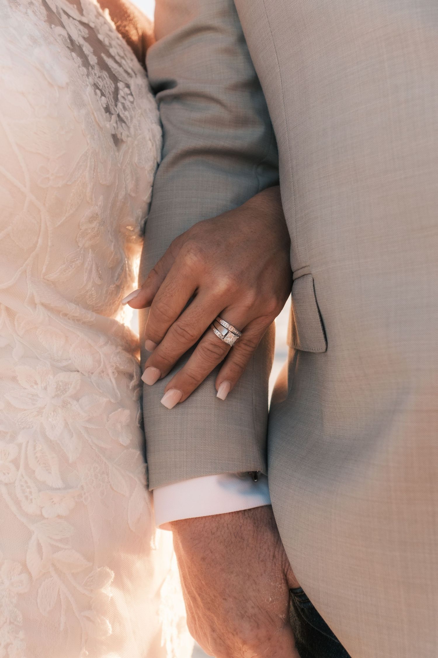 Close-up of bride's hand resting on groom's arm, showcasing a sparkling diamond wedding ring.