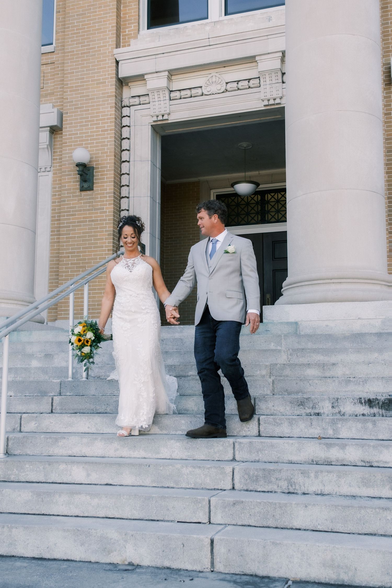 Bride and groom holding hands walking down stone steps outside a historic church after their wedding ceremony.