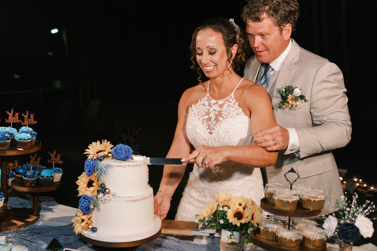 Bride and groom cutting white wedding cake decorated with blue and yellow flowers.
