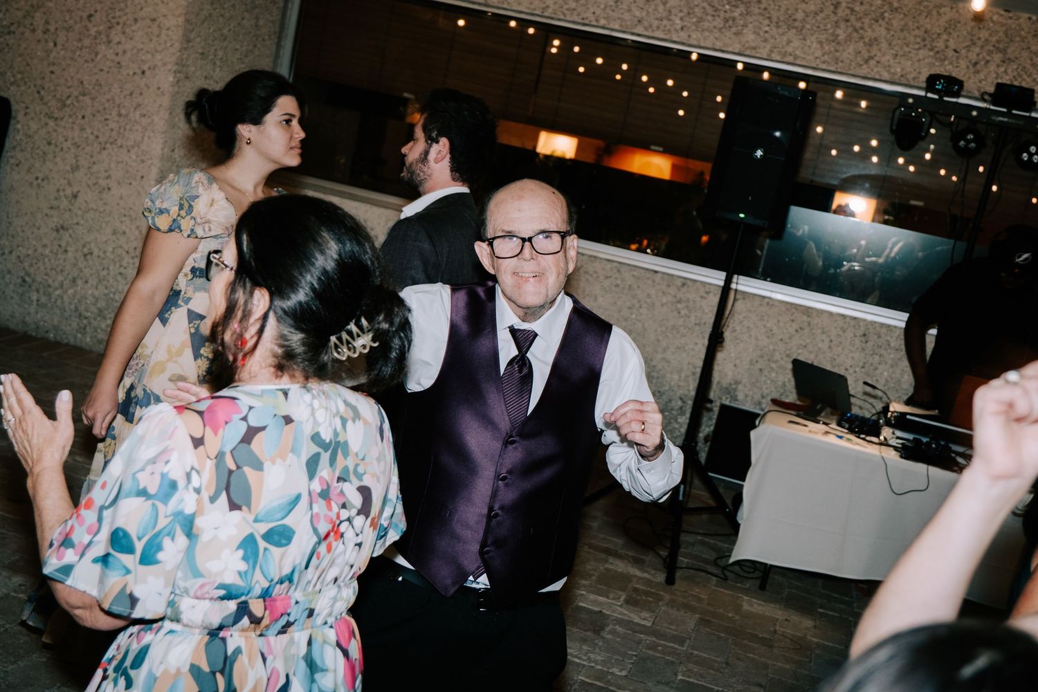 Wedding guests dancing and celebrating on a dimly lit dance floor with string lights overhead.