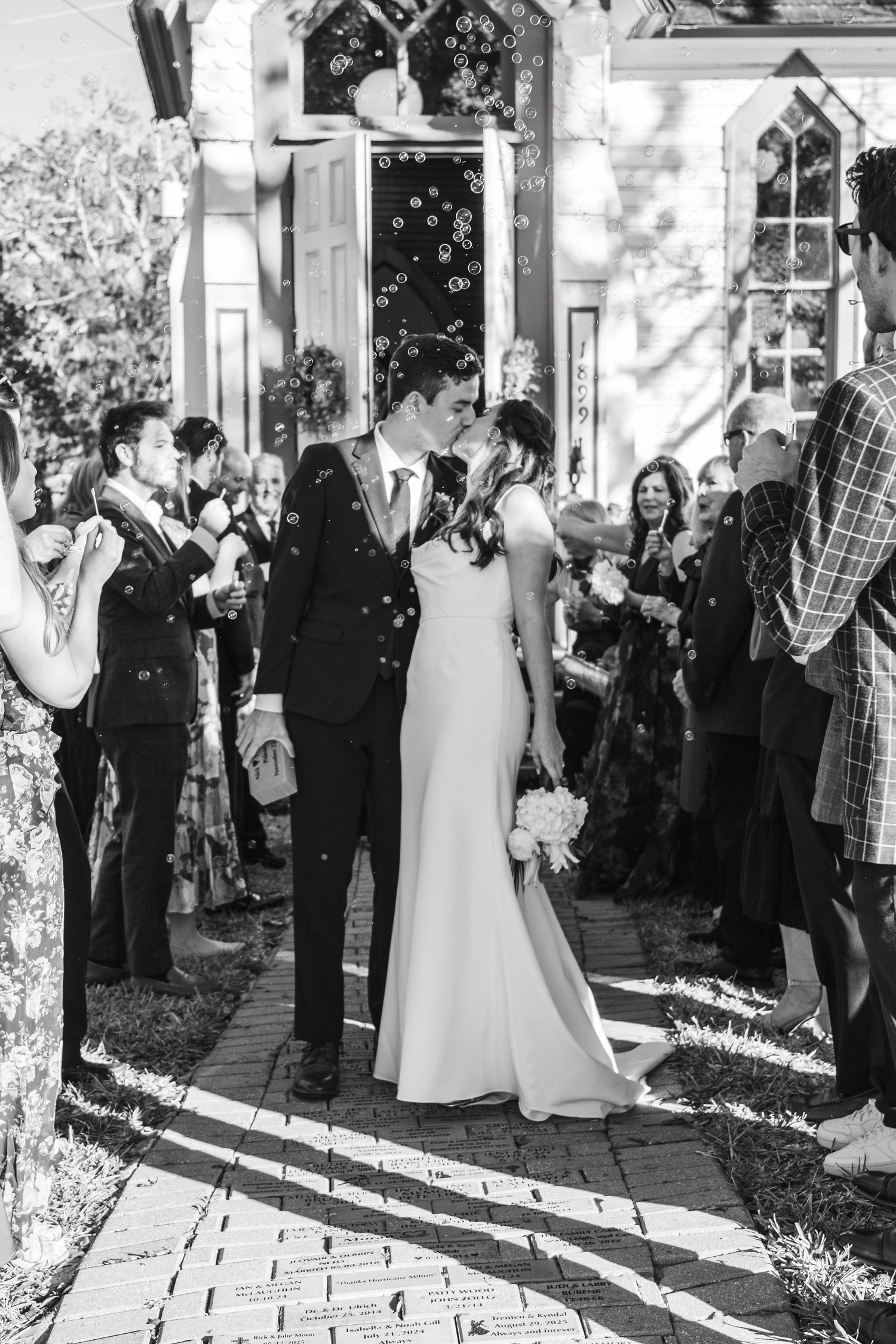 Newlyweds celebrate with guests outside a chapel as bubbles float through the air.