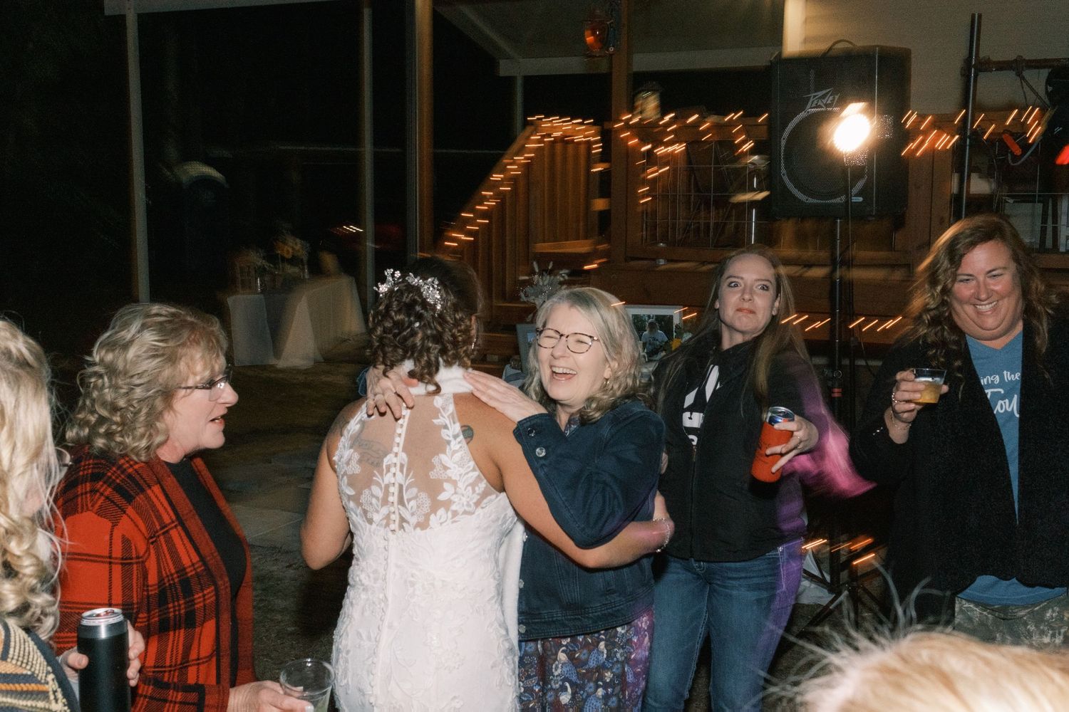 Wedding guests hugging bride in lace gown at outdoor evening reception celebration.