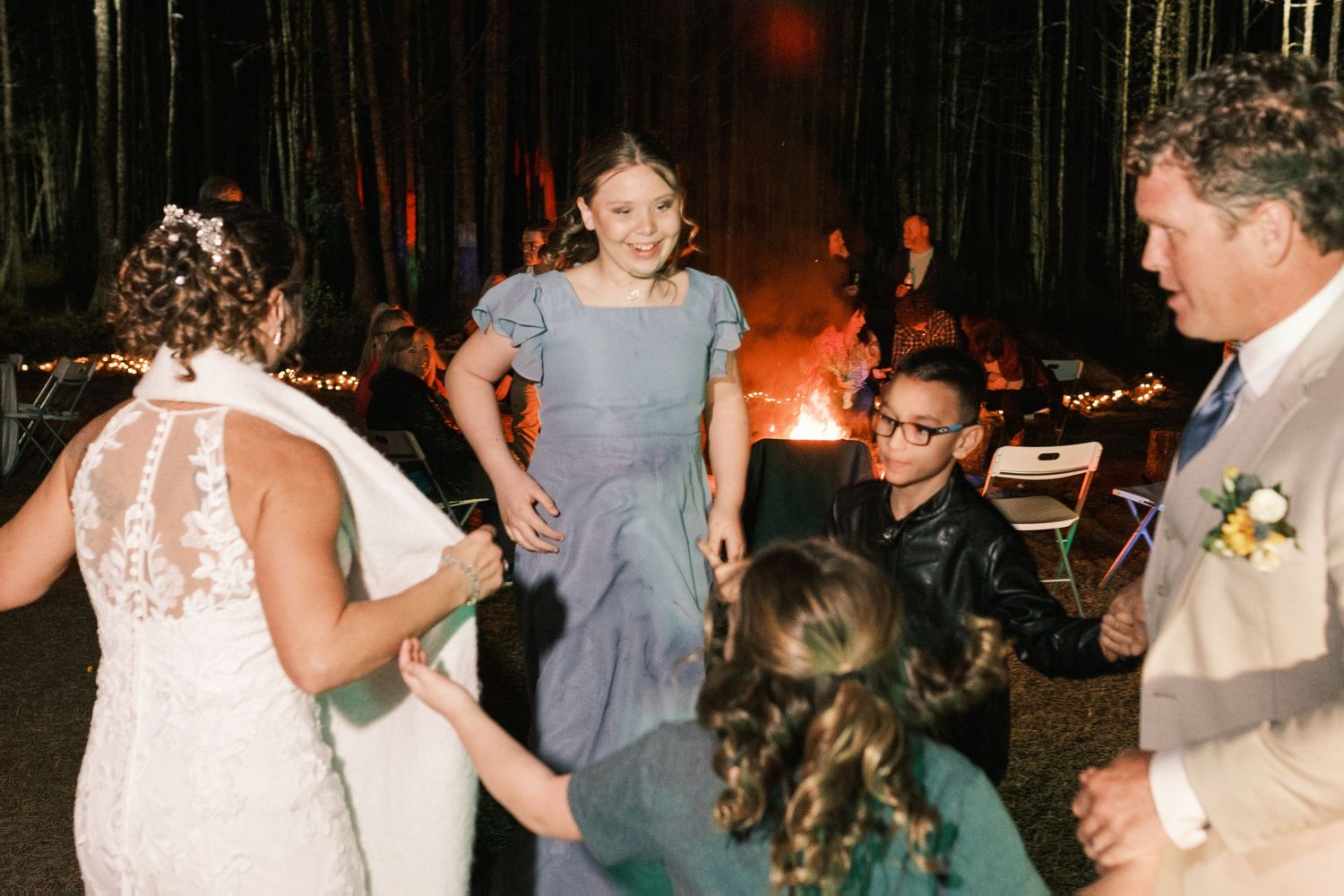 Bride and bridesmaid dancing near a bonfire at an outdoor nighttime wedding reception.