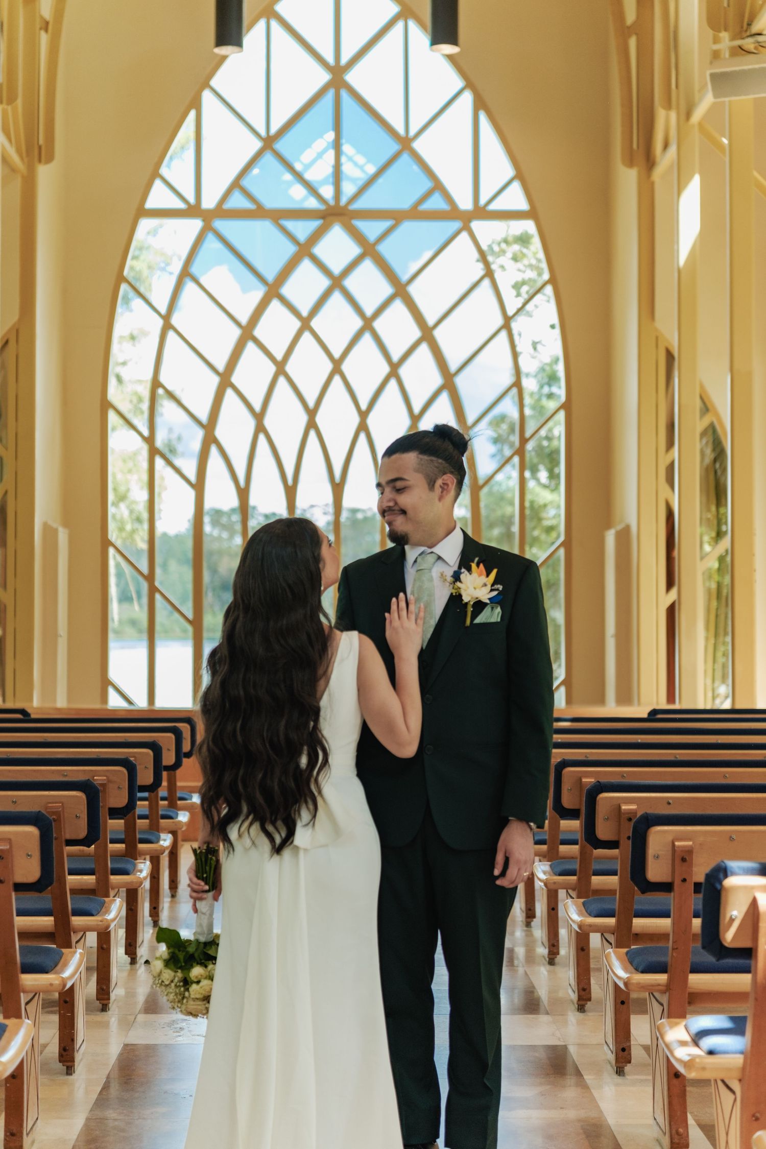 Wedding couple interacts playfully in a modern chapel with geometric windows.