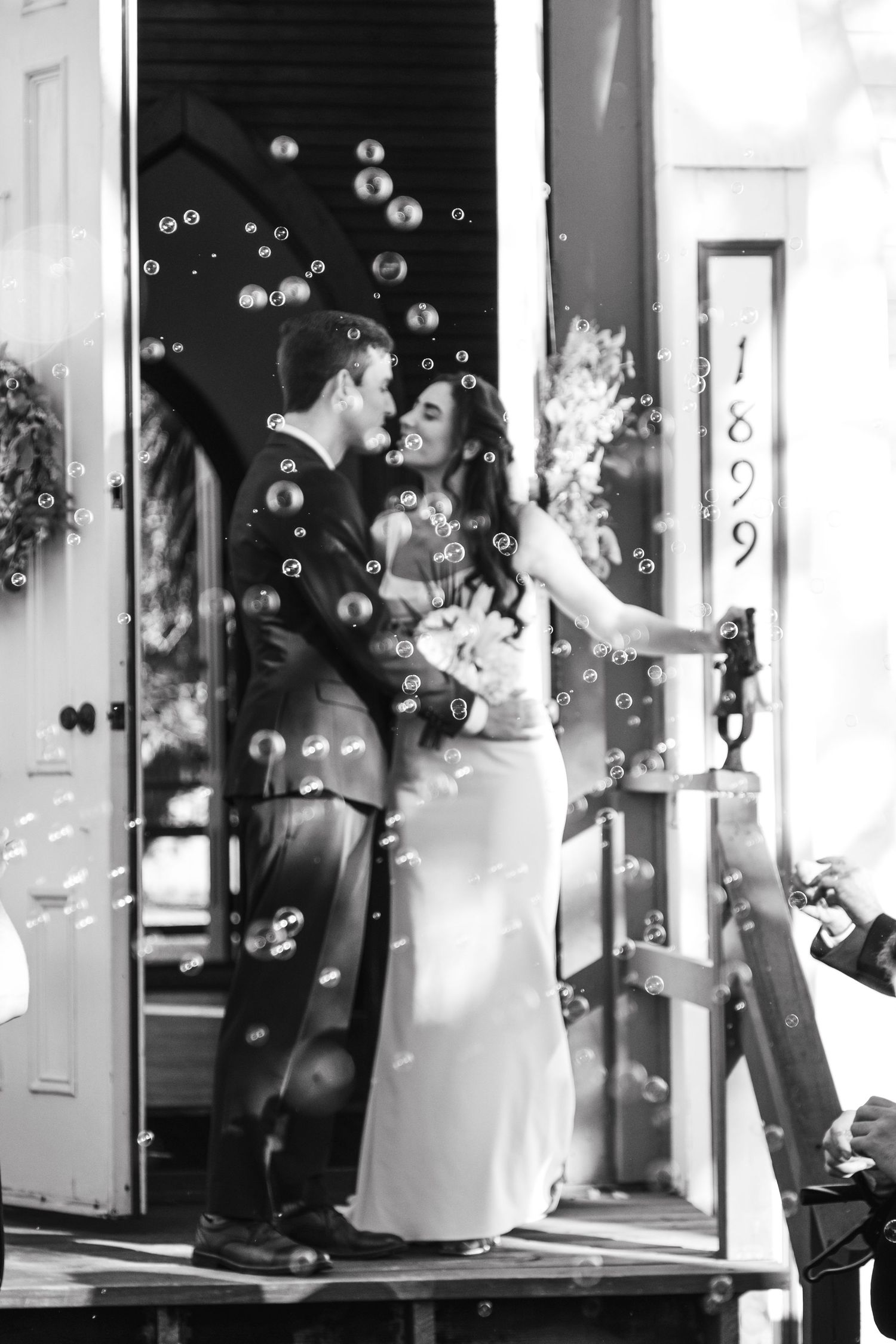 Joyful wedding celebration with bubbles floating in the air outside a white building entrance.