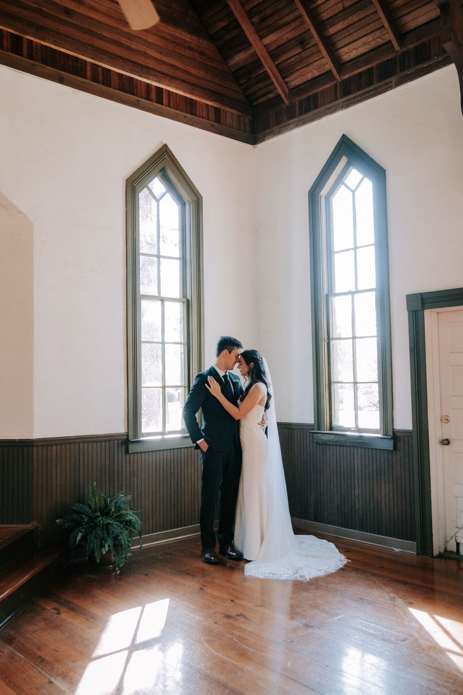 Wedding couple shares intimate moments in a rustic chapel with gothic windows and wooden floors.