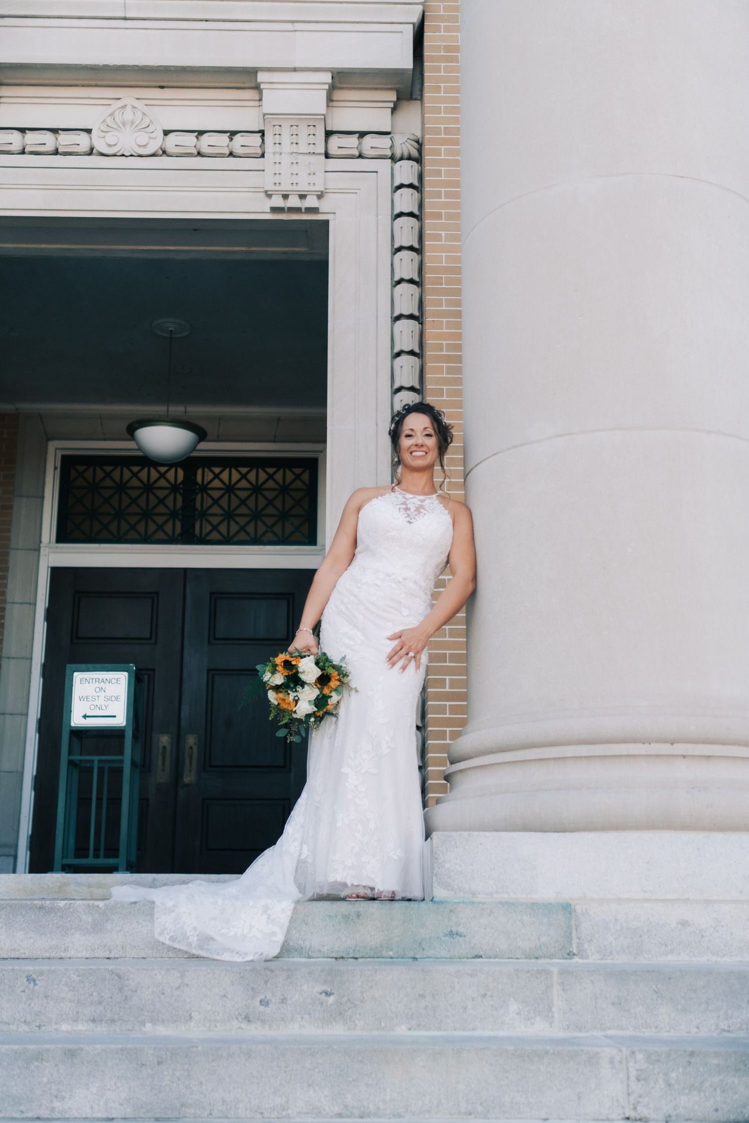 Bride in white lace mermaid gown holding bouquet on church steps.