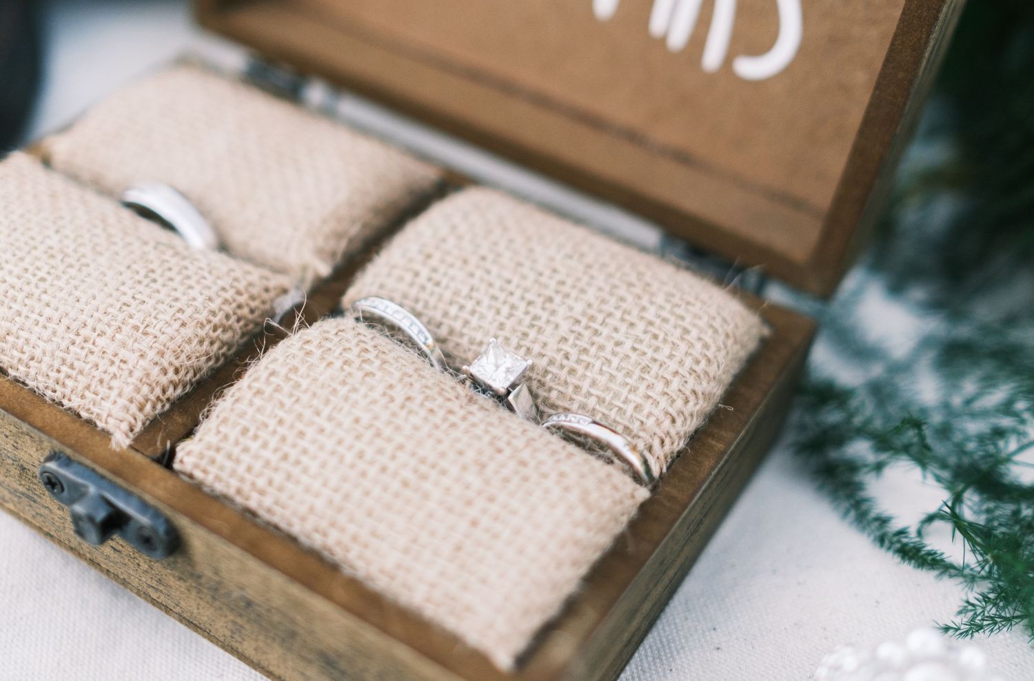 Two silver wedding bands displayed in a rustic wooden ring box with burlap cushions.