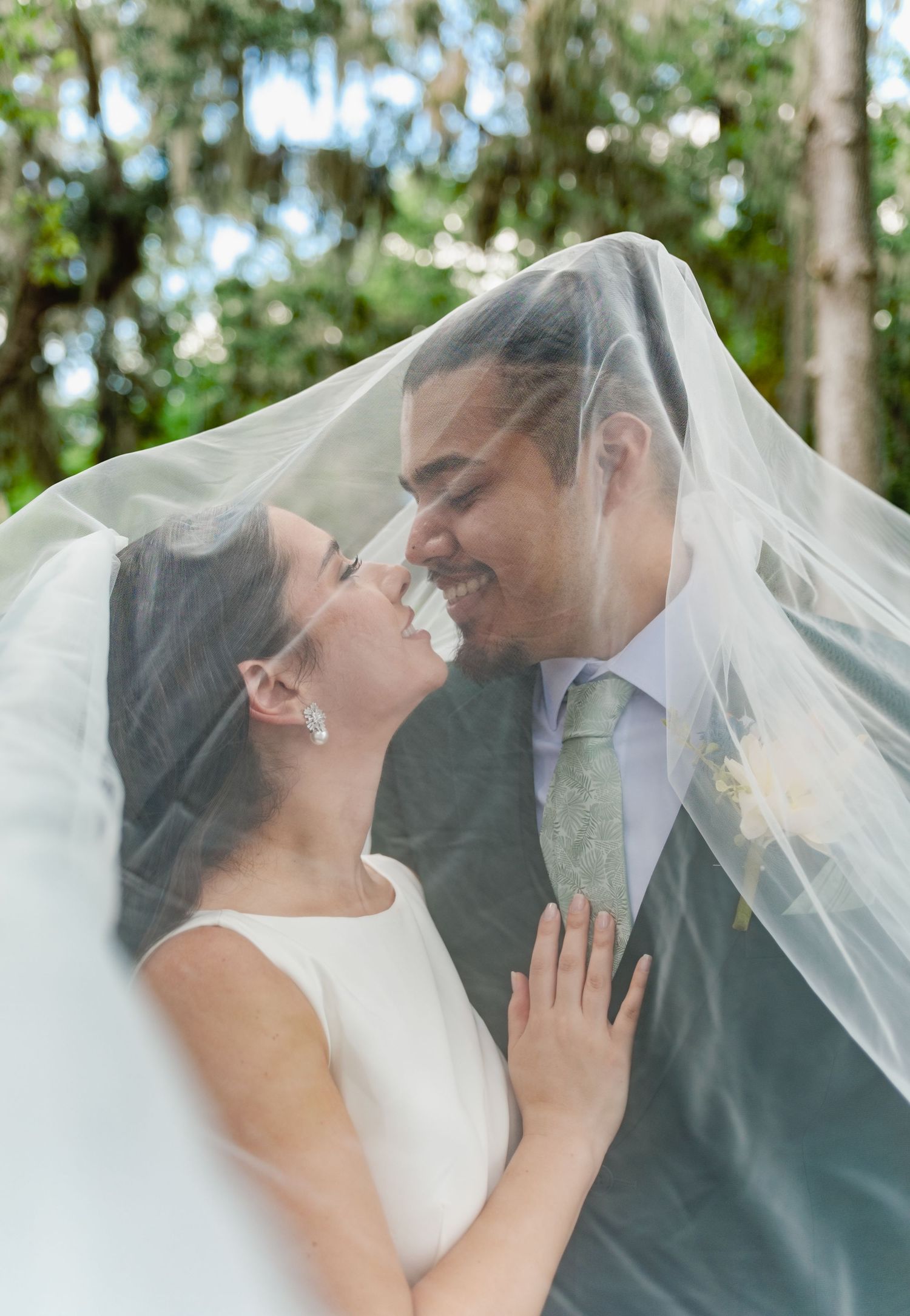 Romantic moment captured under a flowing veil in a natural outdoor setting.