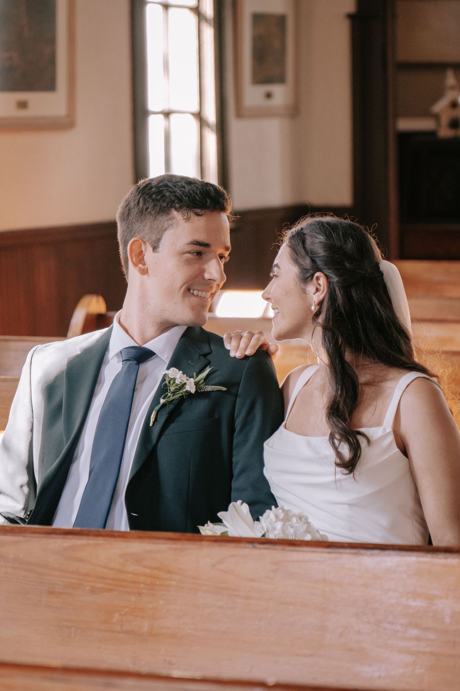 Romantic wedding couple shares intimate moments while sitting at a wooden table in an indoor venue.