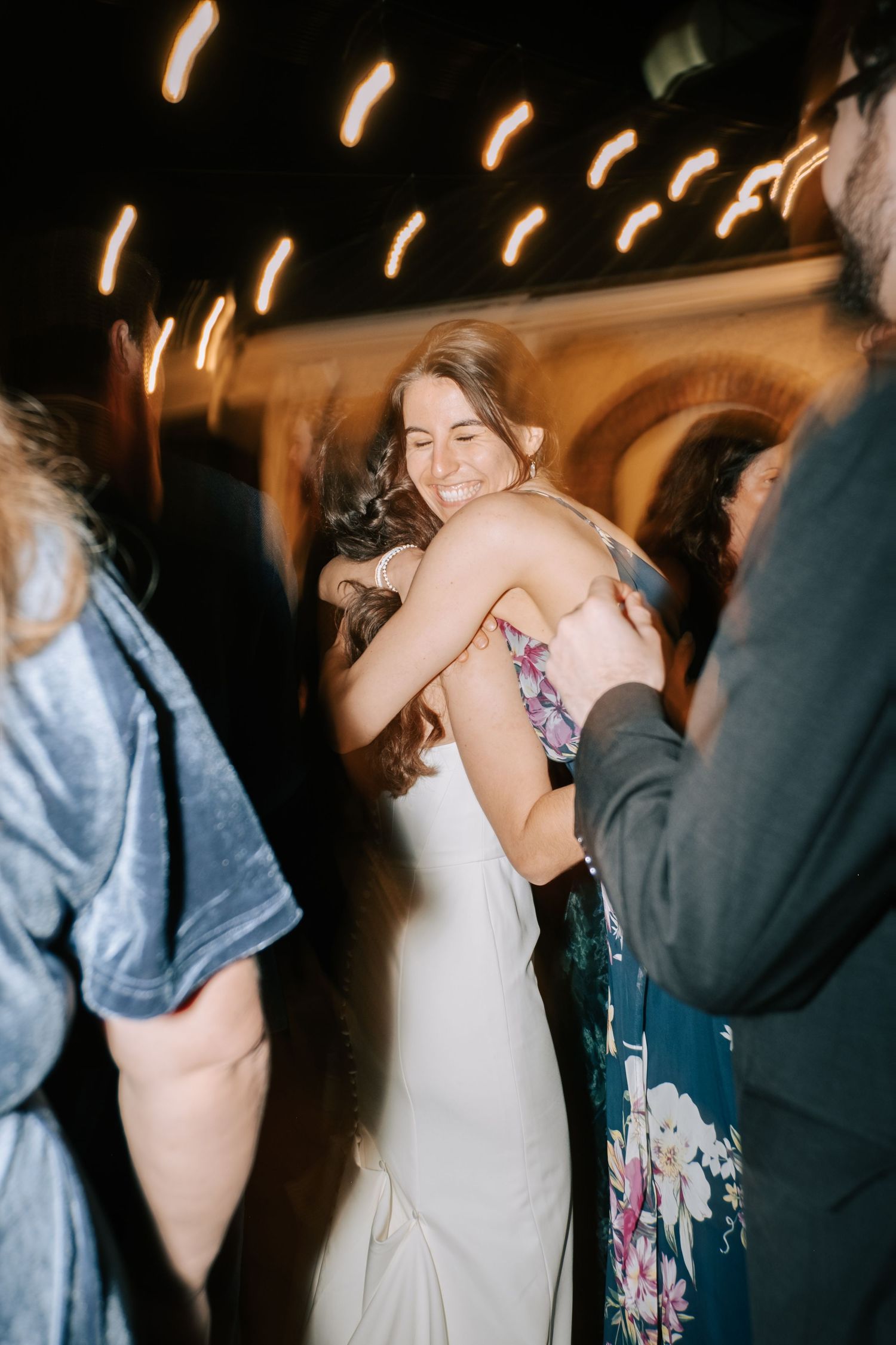 Lively dance floor moments at wedding reception with string lights overhead.