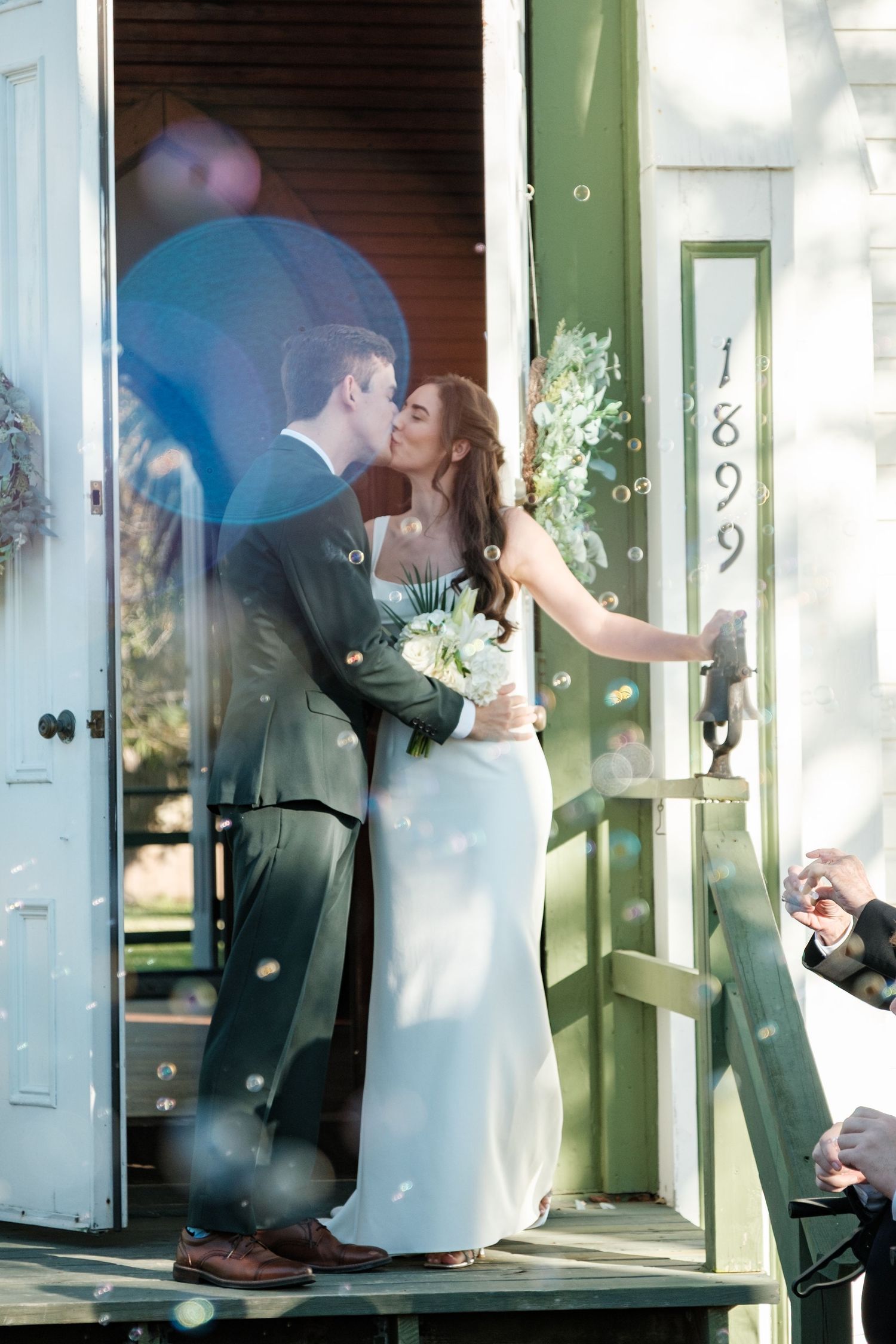 A romantic moment captured on a porch as newlyweds share their first kiss by a green door.