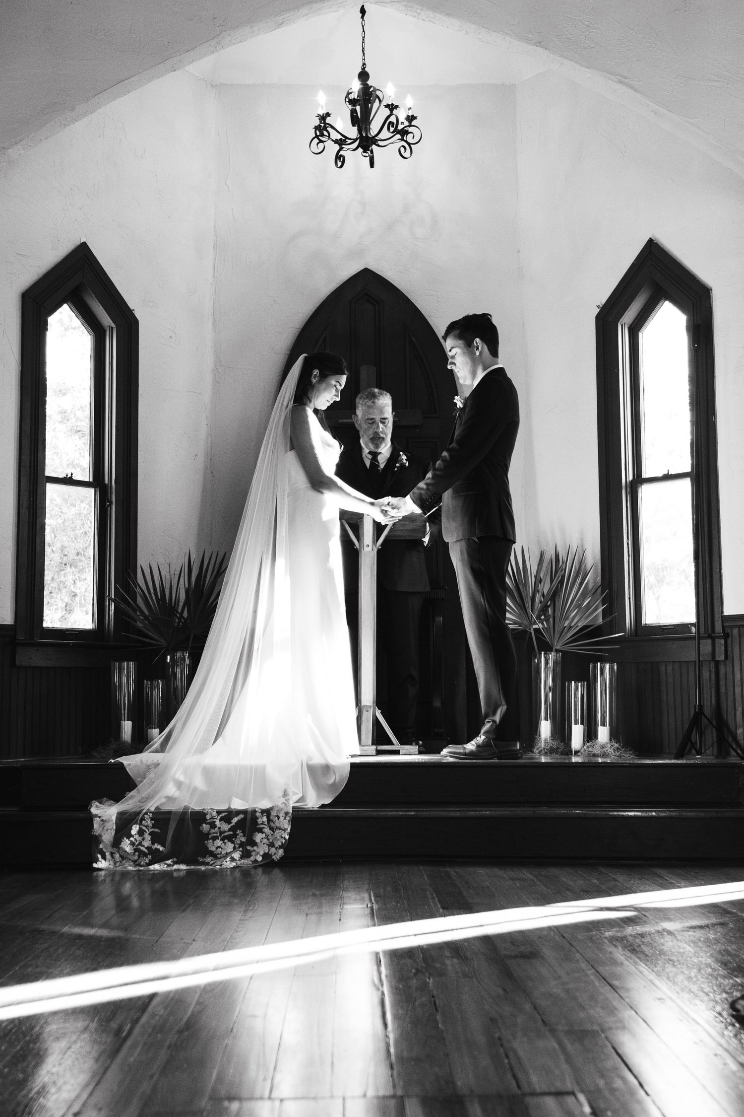 Black and white wedding photos in a chapel with dramatic Gothic windows and natural light streaming in.