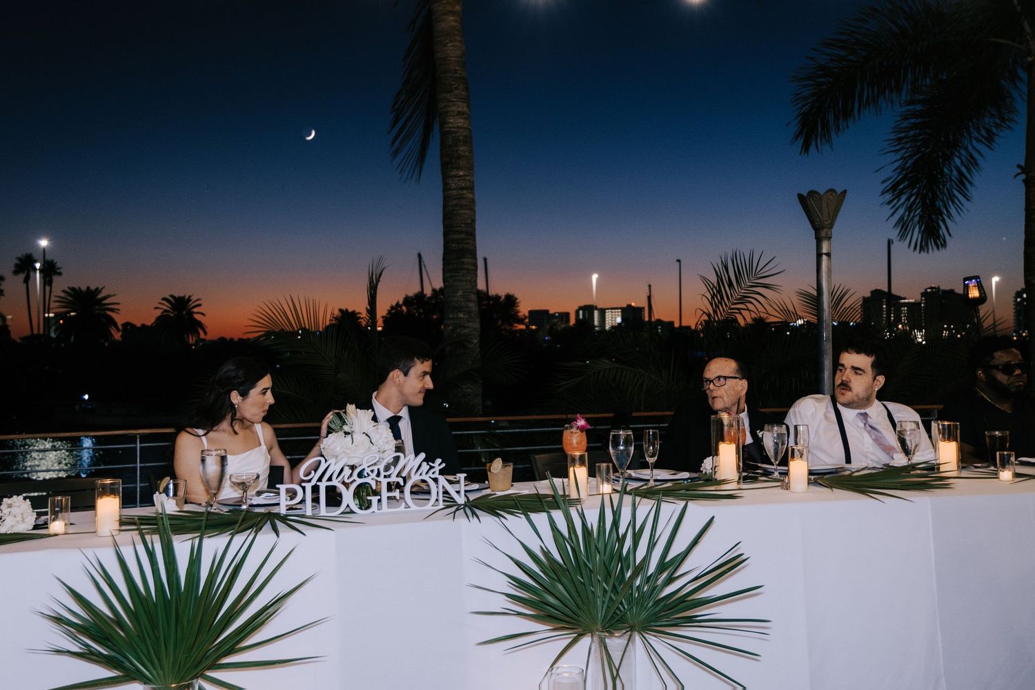 Evening wedding reception panorama under palm trees with string lights.