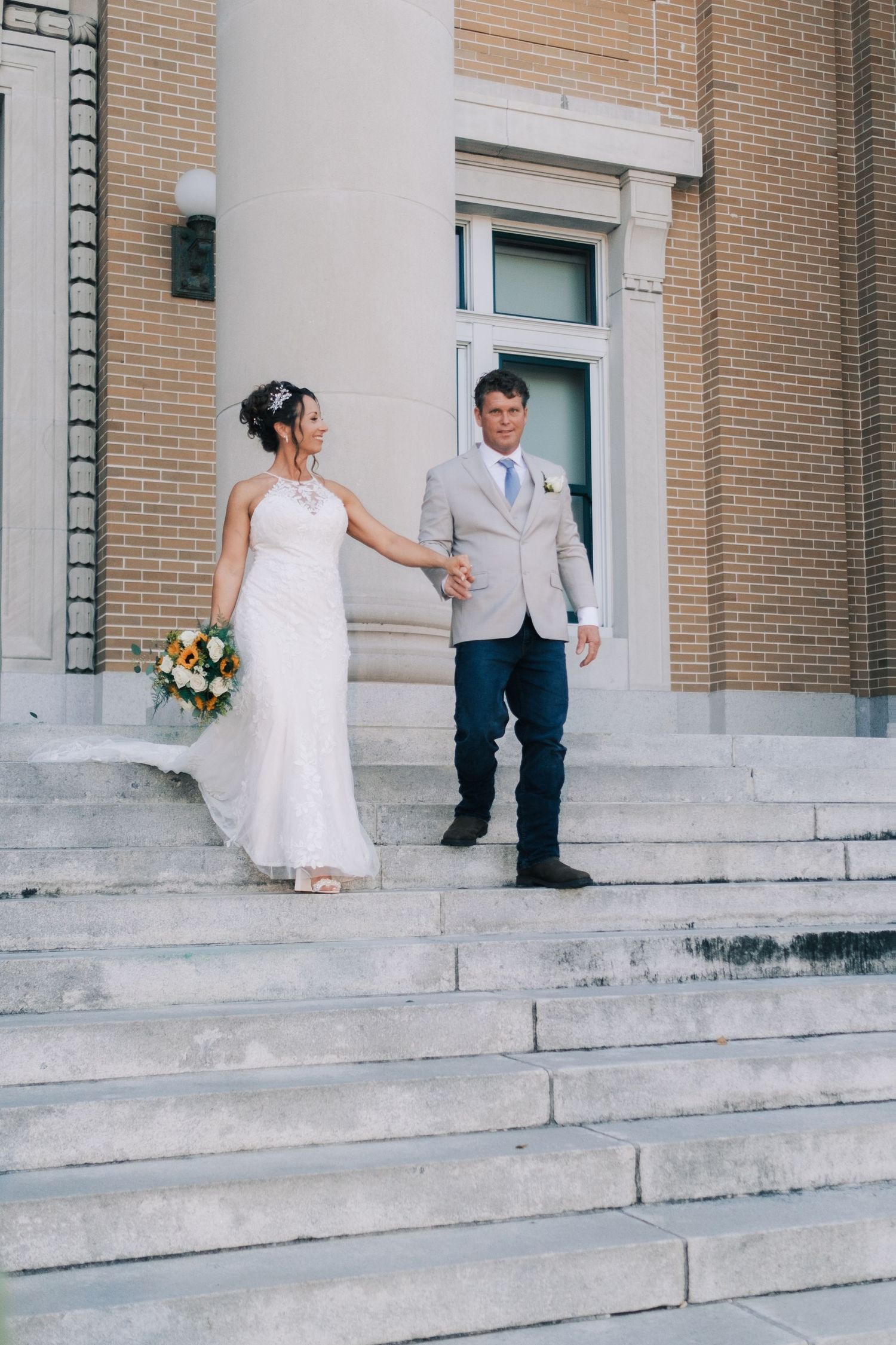 Bride and groom holding hands walking down stone steps of elegant building on wedding day.
