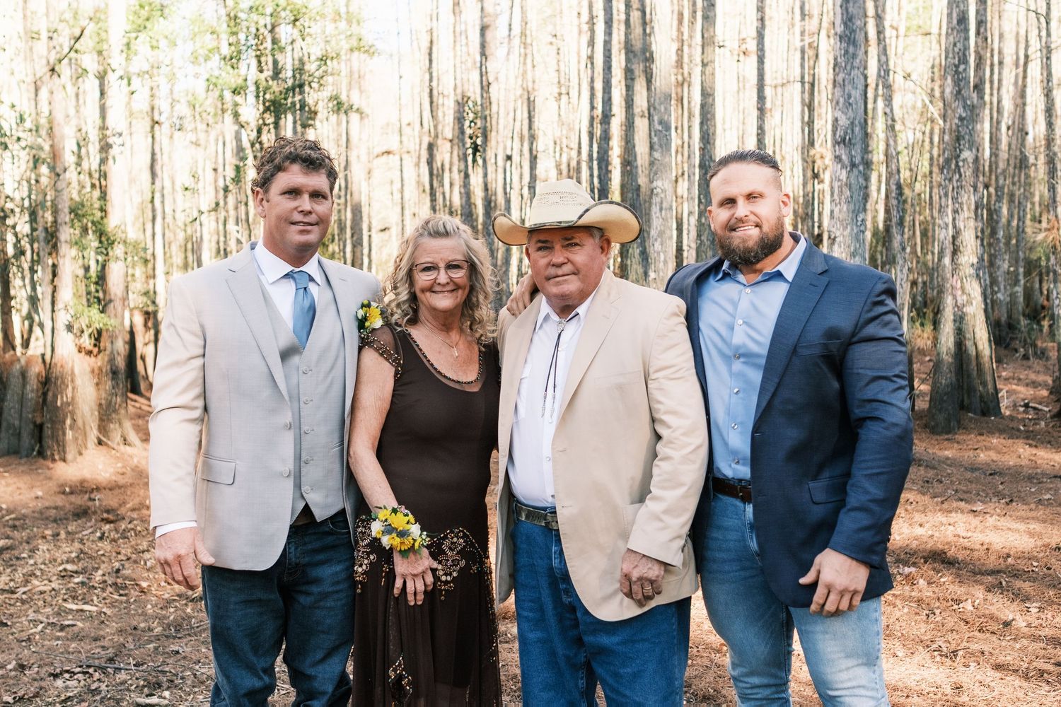 Family group portrait of four people in formal attire posing in pine tree forest.