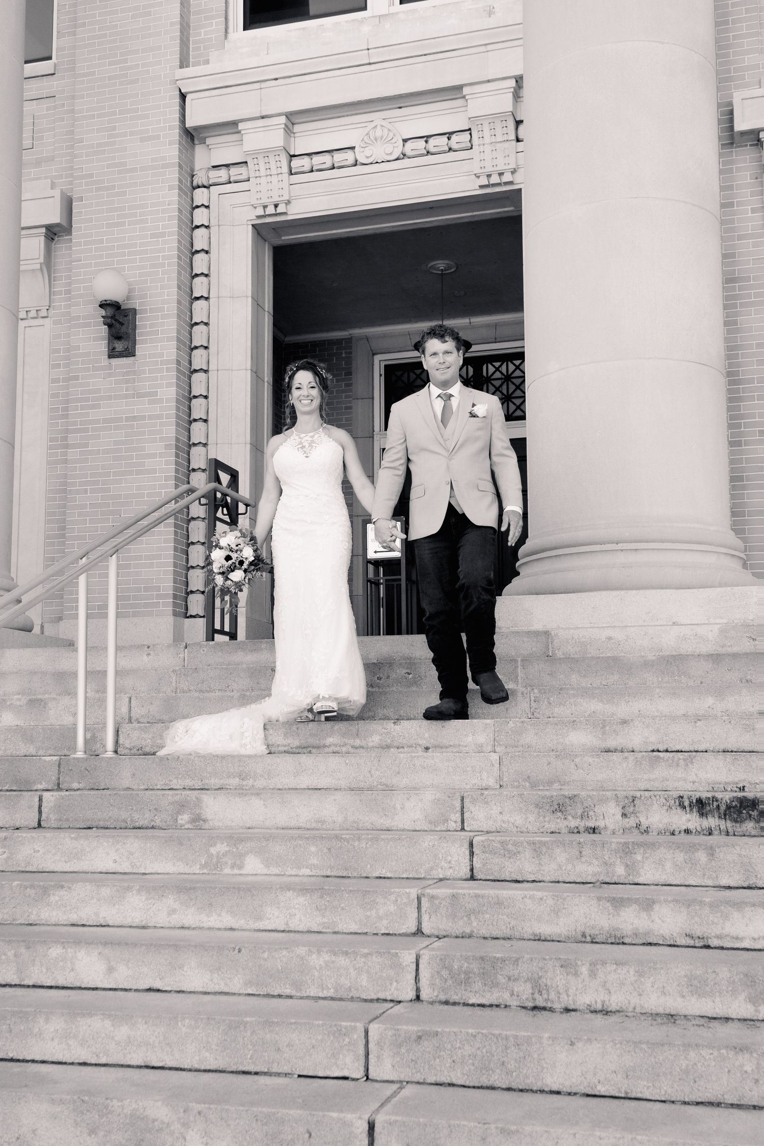 Bride and groom holding hands walking down stone steps of historic building after ceremony.