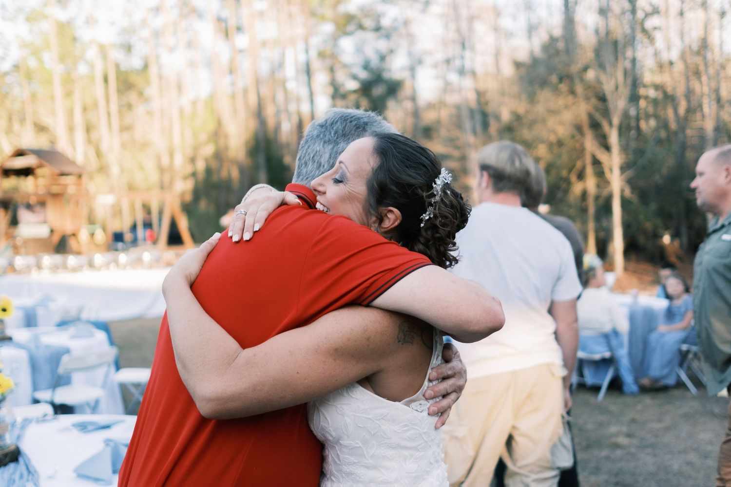 Bride shares a heartfelt hug with a guest at an outdoor woodland wedding reception.