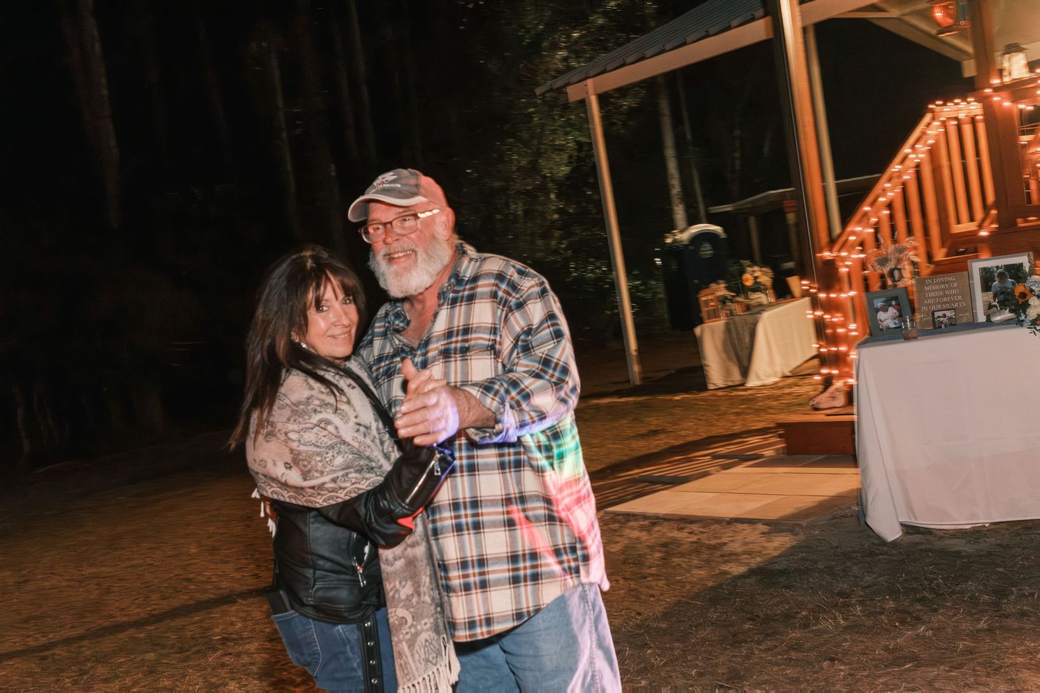 Couple embracing and dancing together at outdoor evening wedding reception with string lights.