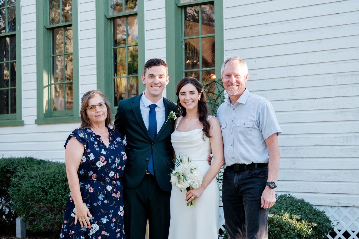 Wedding party poses for formal portraits in front of a white historic building with green trim.