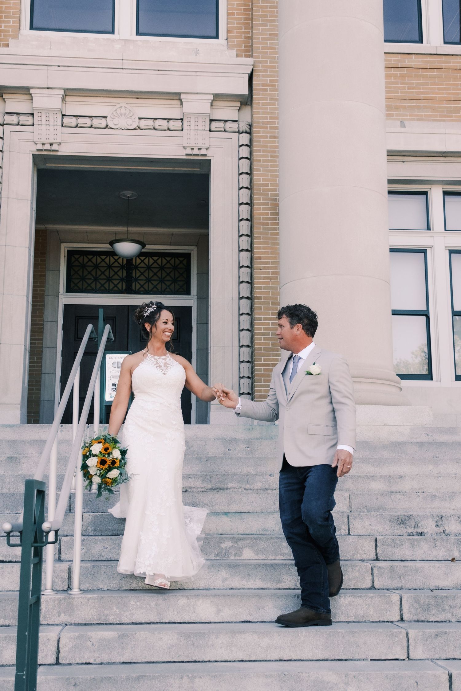 Bride and groom hold hands on steps of elegant building on their wedding day.