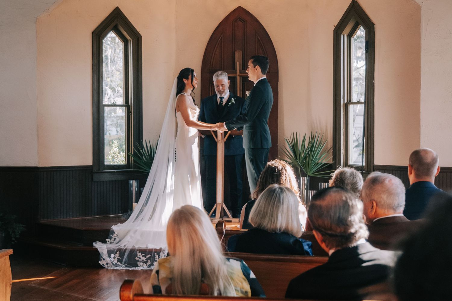 Wedding ceremony inside historic chapel with arched windows and wooden details.