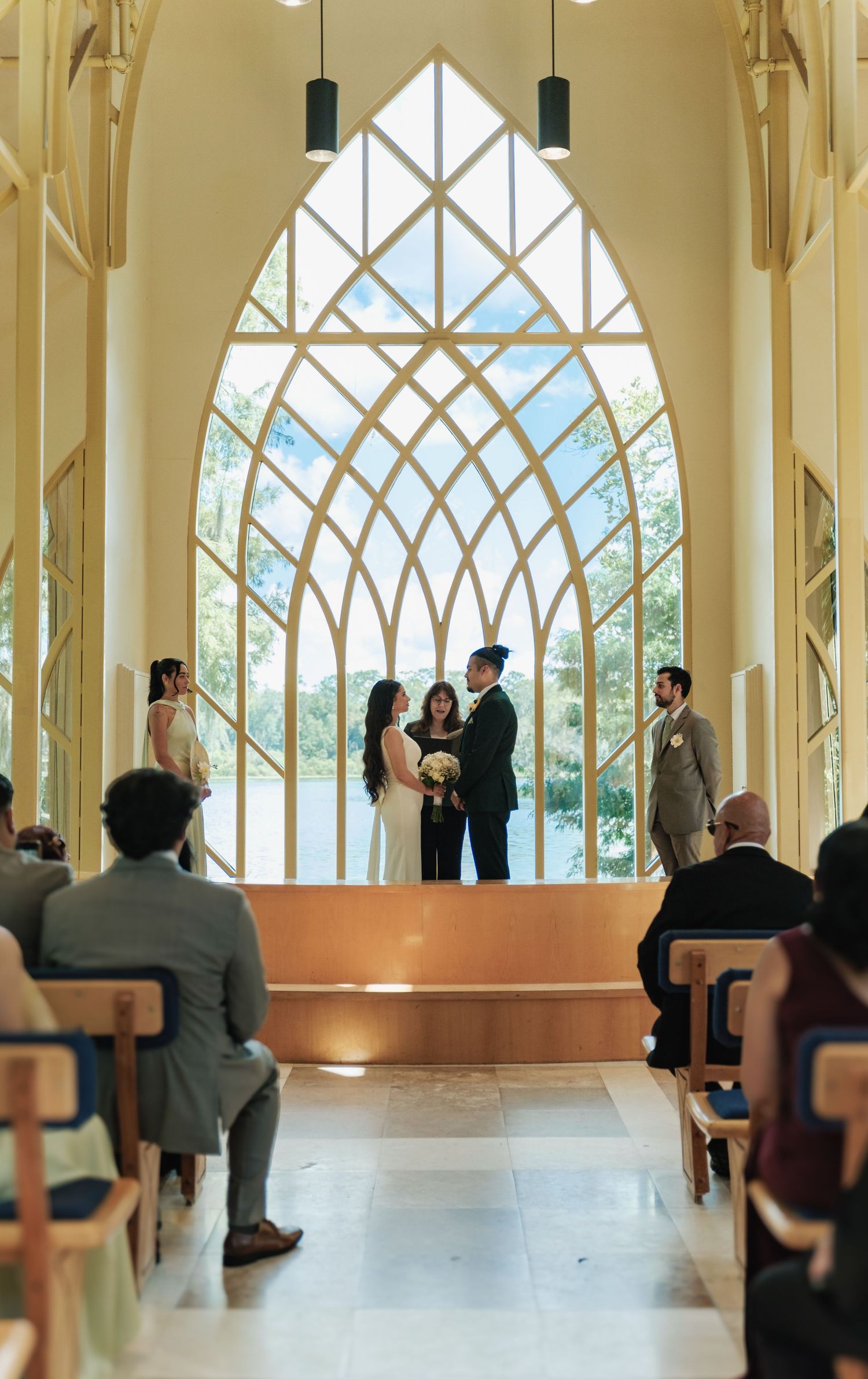 Wedding ceremony taking place in a chapel with a stunning geometric window and natural light streaming in.