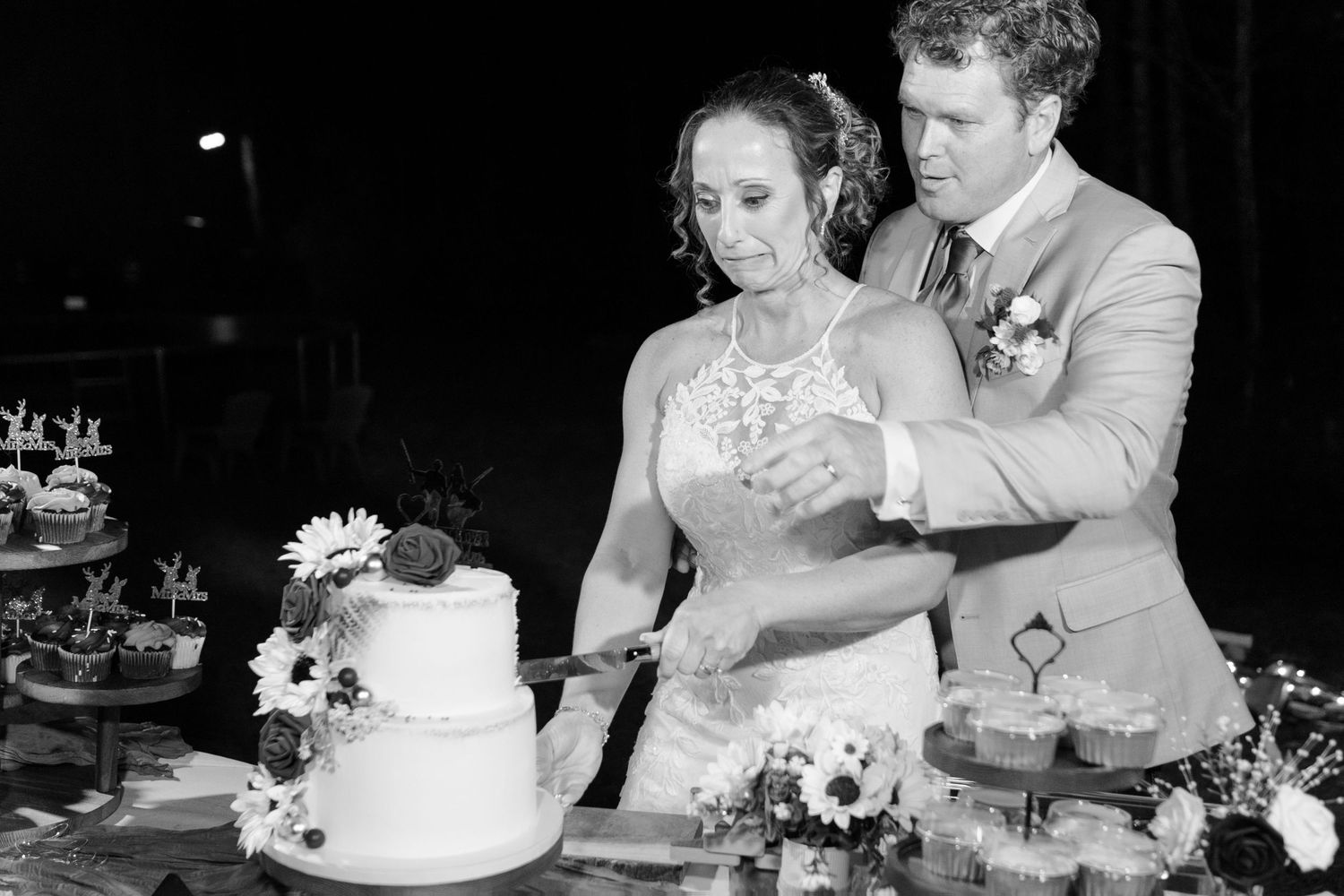 Bride and groom cut their two-tier wedding cake surrounded by floral decorations in black and white photo.