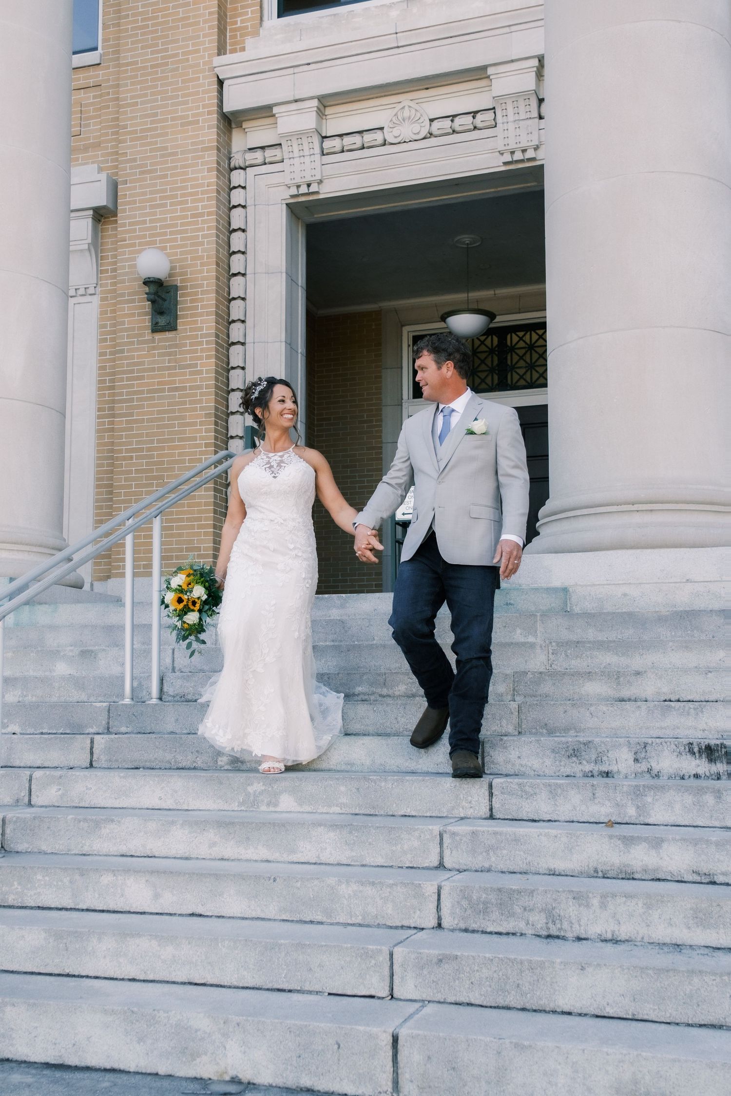 Bride and groom holding hands walking down stone church steps after wedding ceremony.