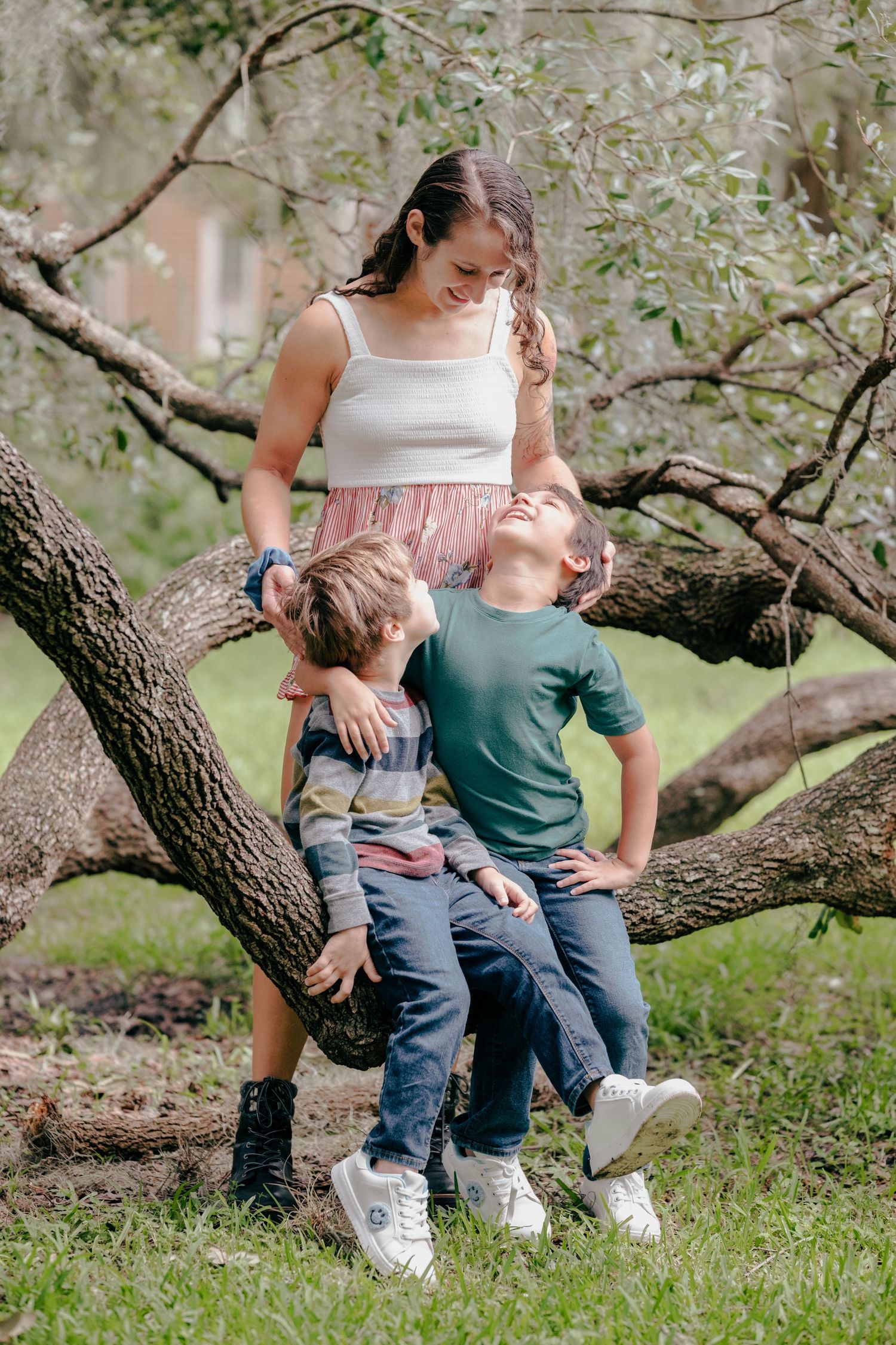 A family sits together on a fallen tree branch in a peaceful outdoor setting during a photo session.