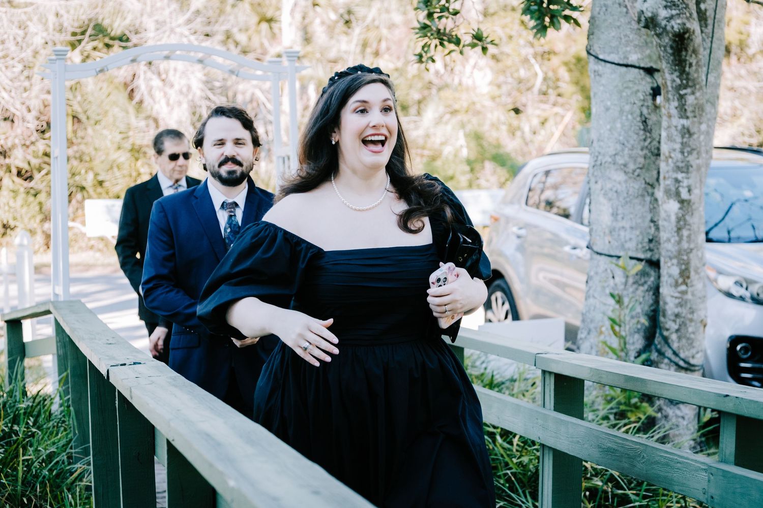 A joyful moment captured on a wooden walkway with three people in formal attire enjoying themselves outdoors.